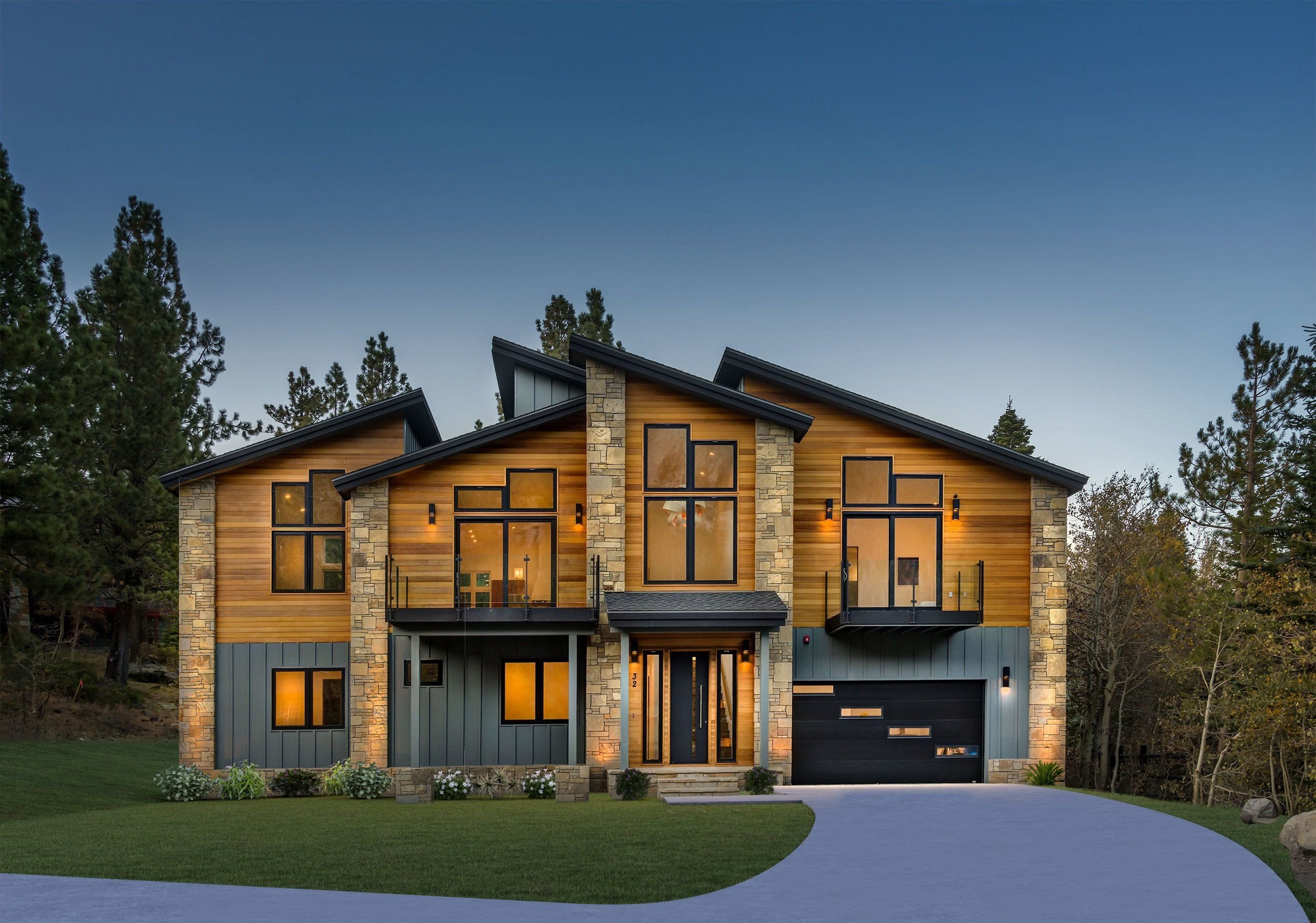 A modern house with large windows and a combination of wood and stone exterior, set against a backdrop of tall pine trees and a clear sky at dusk.