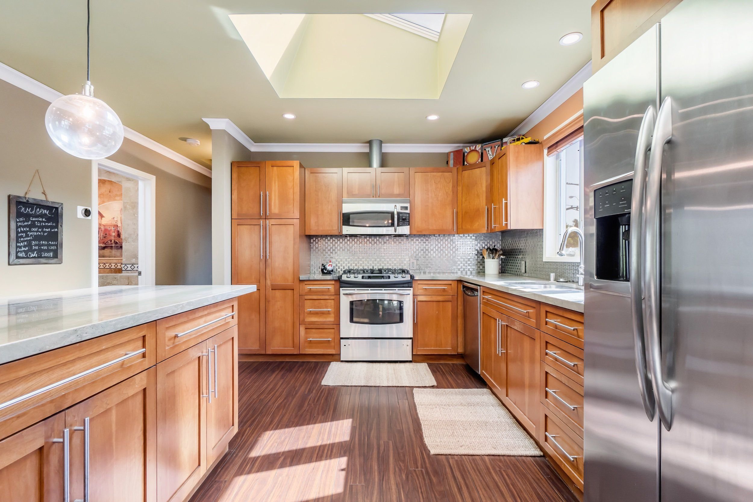 Modern kitchen with wooden cabinets, stainless steel appliances, and a skylight in the ceiling.