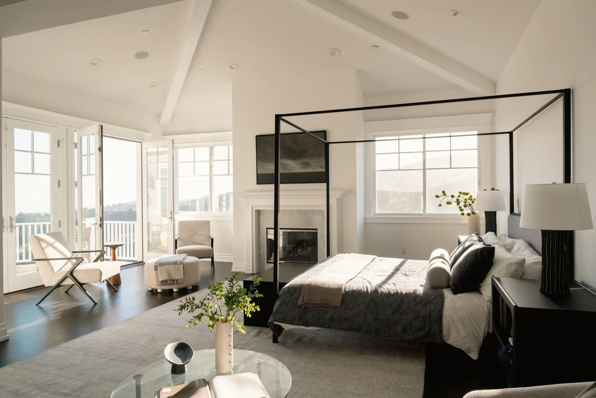 Bright, modern living room with large windows, a fireplace, and minimalistic decor, including chairs, a sofa, and plants.