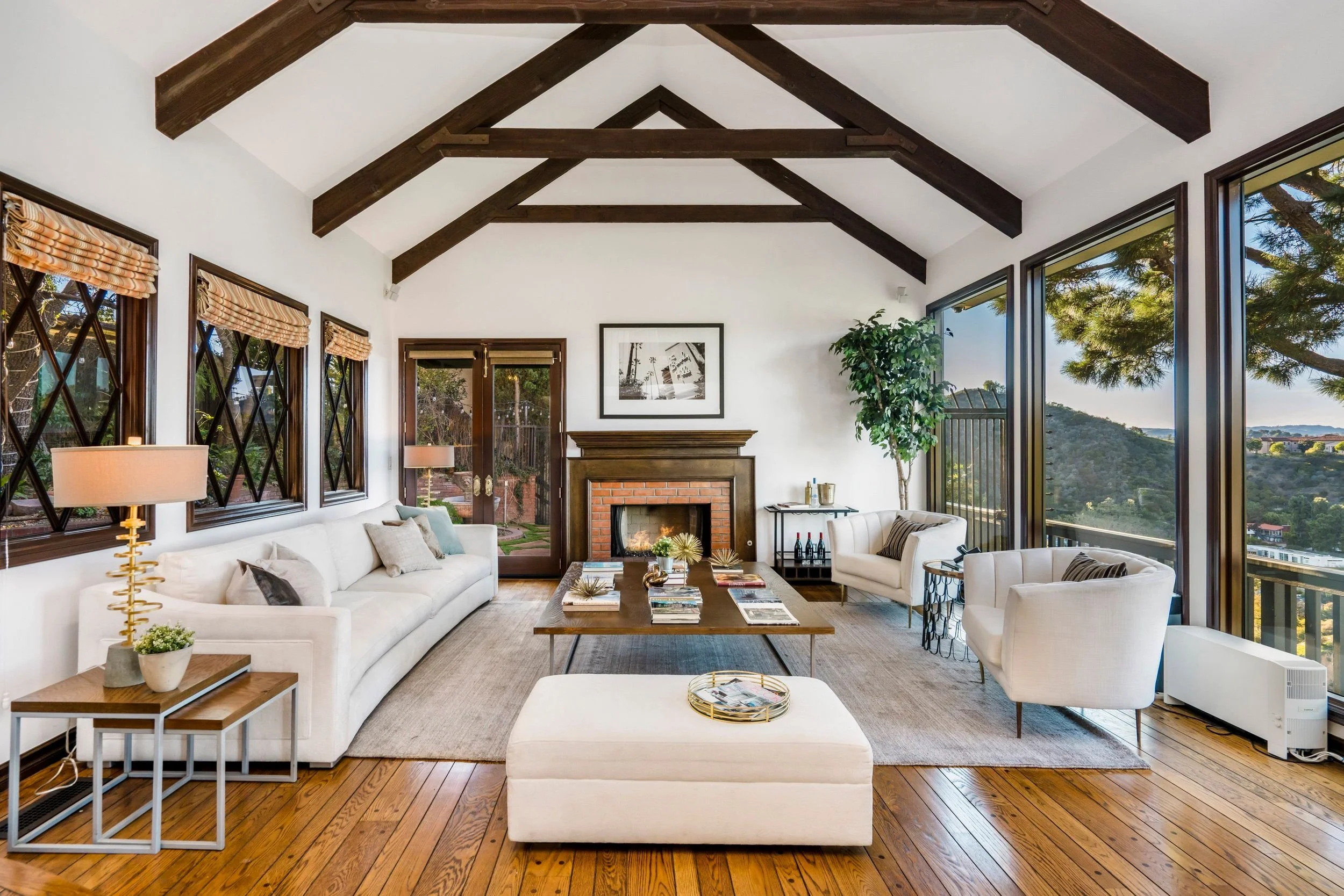 Living room with white sofas, a wooden coffee table, large windows with mountains view, fireplace, and decorative pillows.