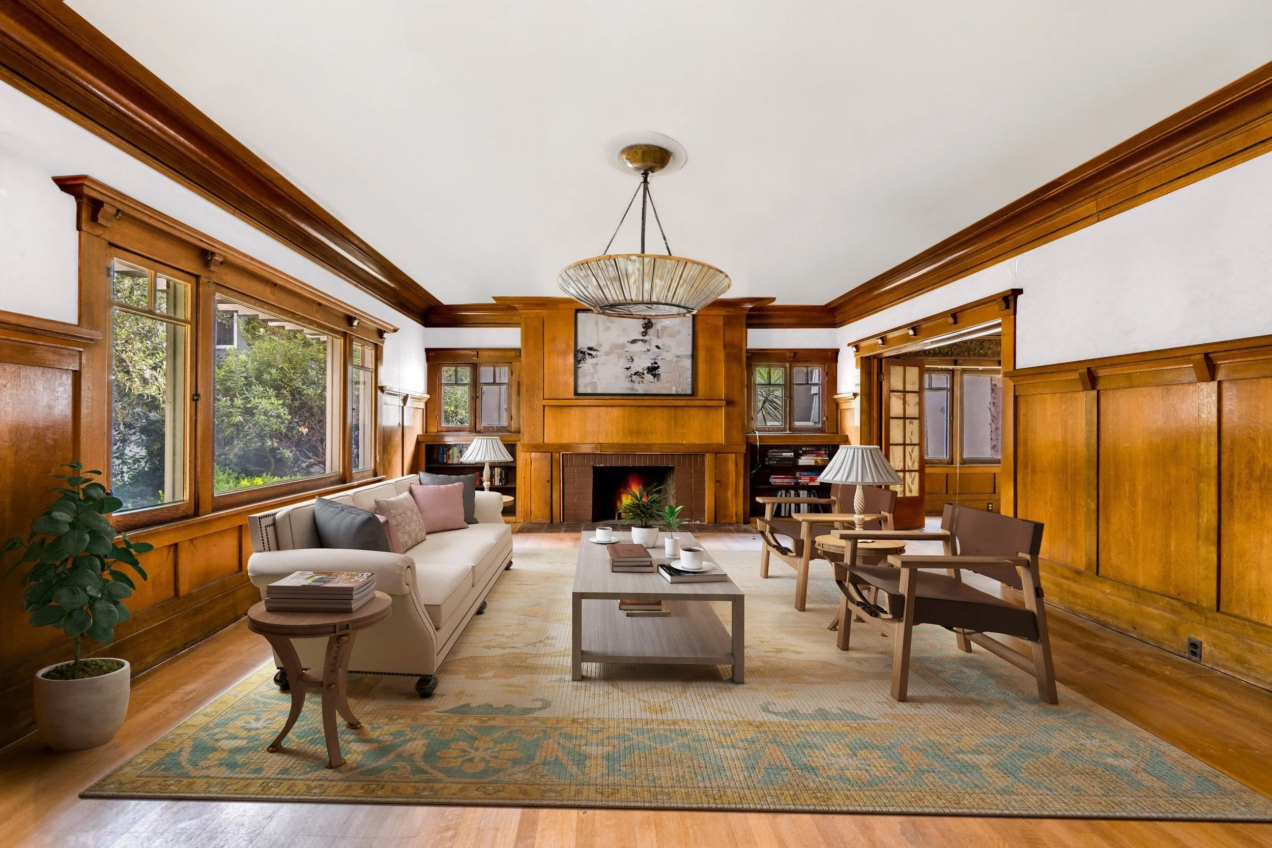 Living room with wooden paneling, a fireplace, large windows, a sofa, armchairs, modern ceiling light, coffee table with books and cups, and large potted plant.