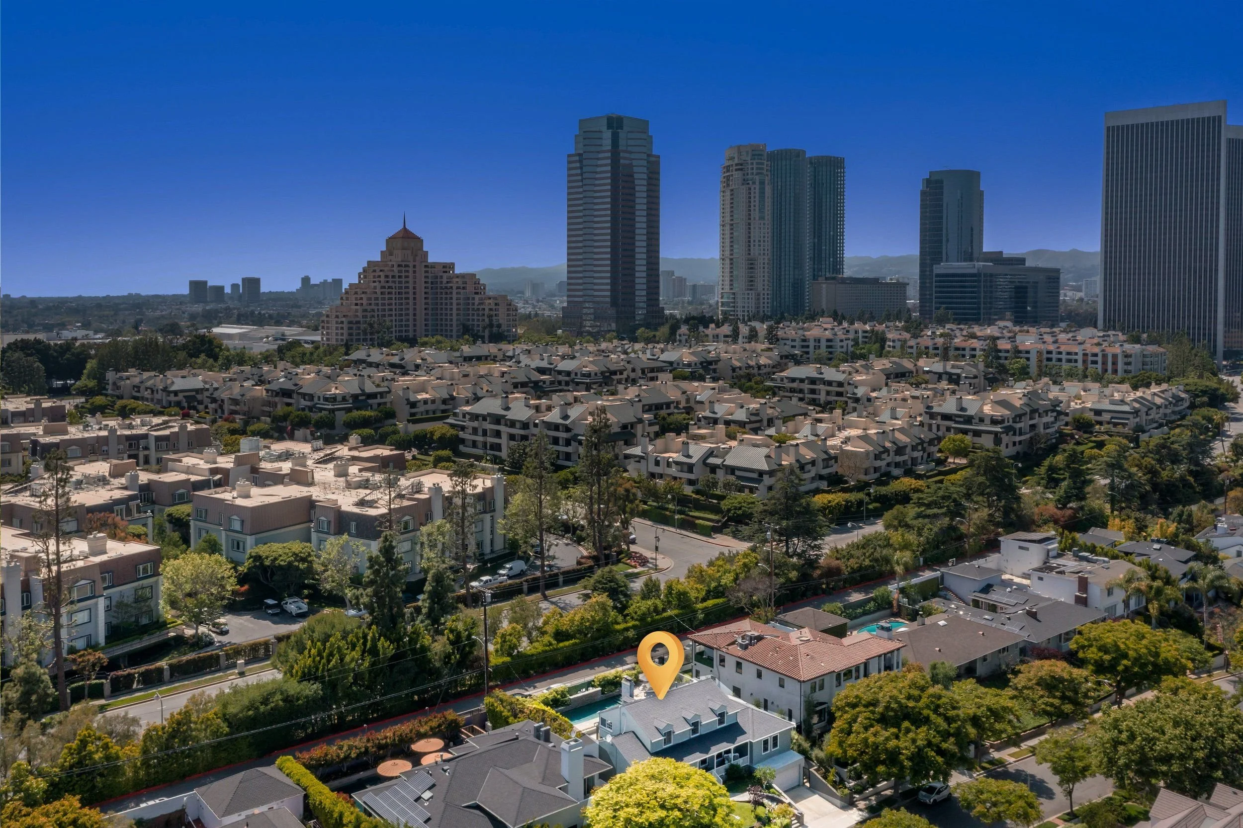 A city skyline with high-rise buildings and residential houses under a clear blue sky.