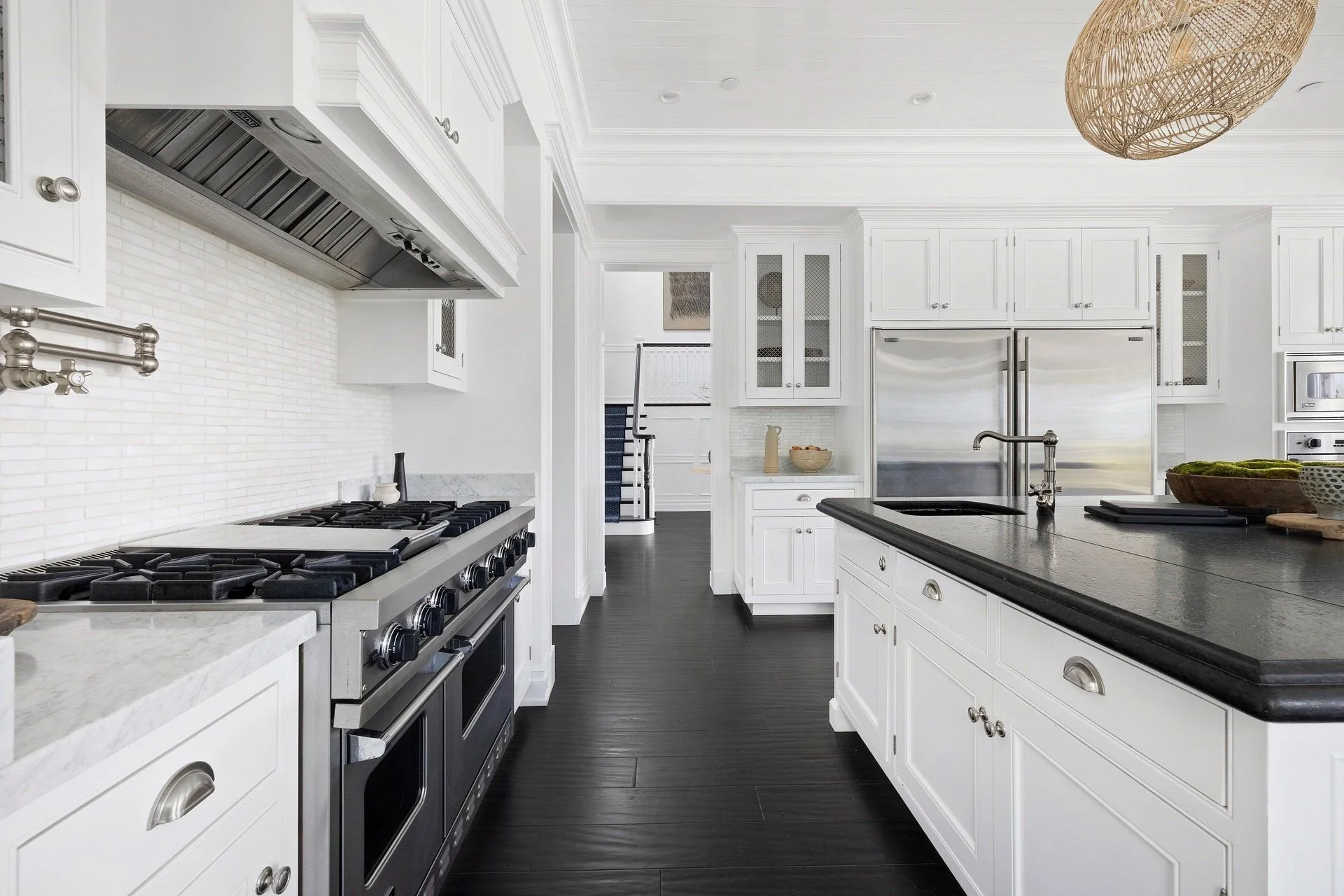 Modern white kitchen with stainless steel appliances, black countertops, and dark wood flooring. Includes a stove, microwave, and a double-door refrigerator.