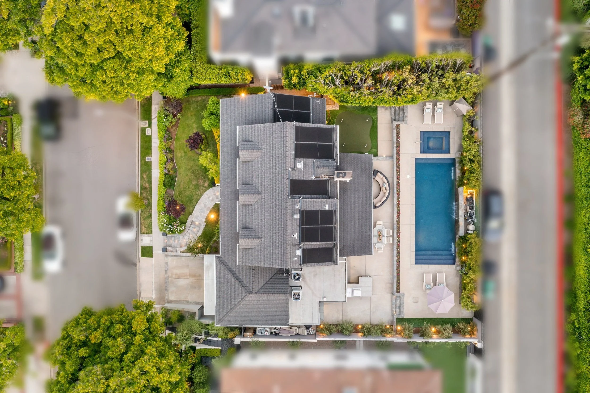 Aerial view of a residential backyard with green lawn, swimming pool, patio, and trees.