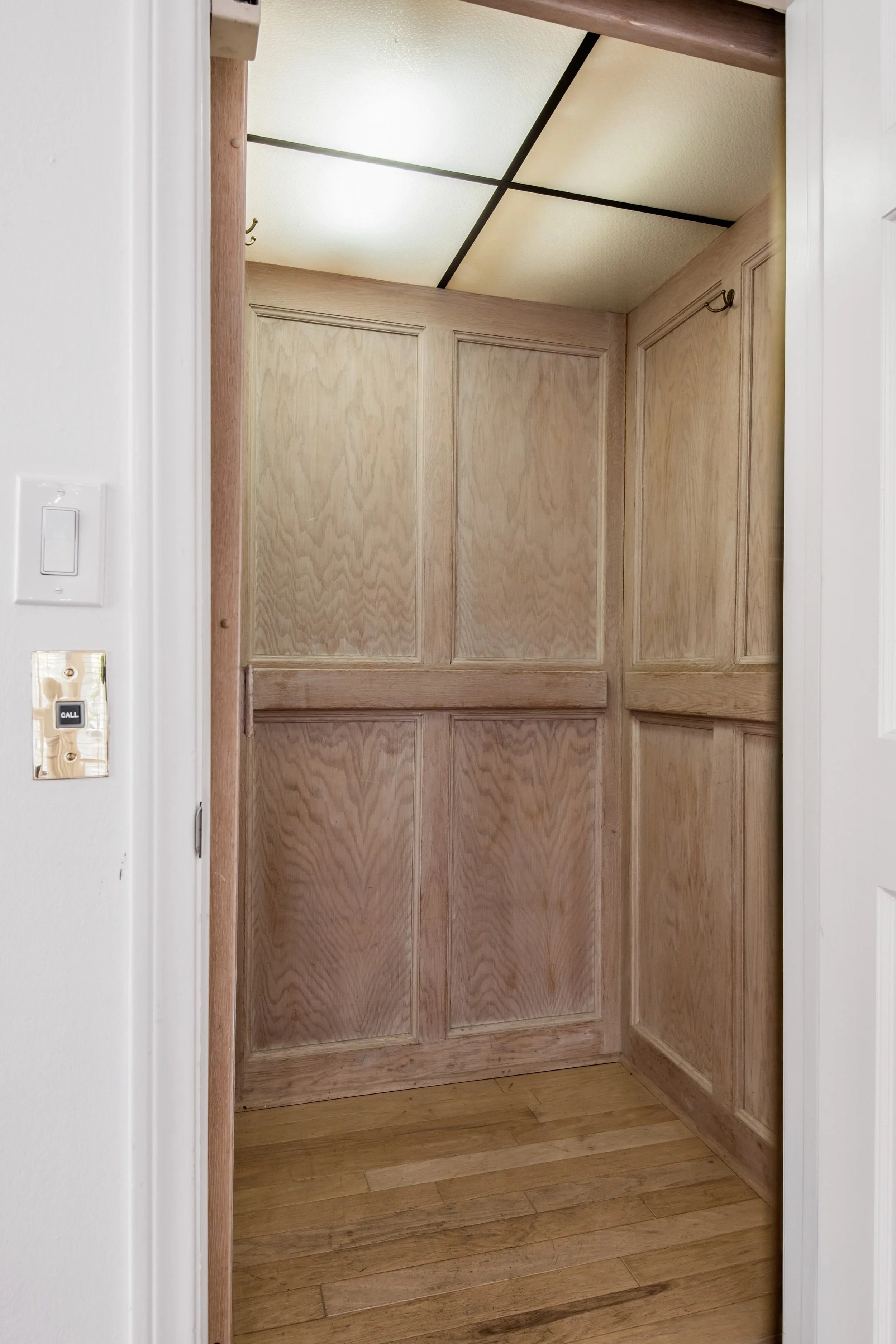 Wooden closet doors with a natural finish inside a home, framed by white walls. A light switch is visible on the left side of the image.