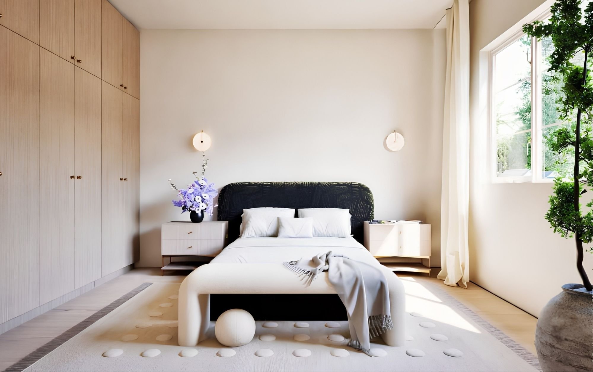 A minimalist bedroom with a white bed, black headboard, and a light wood wardrobe. A nightstand with a purple flower arrangement is beside the bed. Large window with white curtains lets in natural light, and a green plant is on the right side.