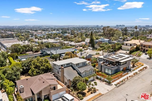 Aerial view of a suburban neighborhood with modern houses, trees, and streets under a blue sky with some clouds.