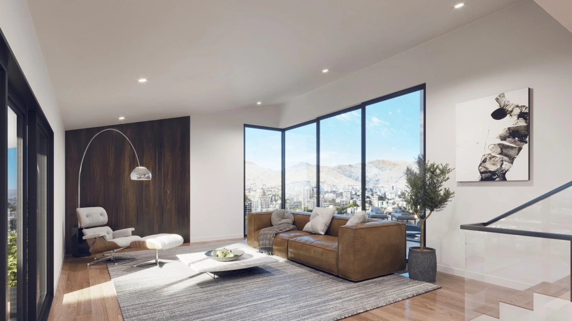 Modern living room with large windows showing city and mountain views, tan leather sofa with pillows, white lounge chair with ottoman, gray area rug, coffee table with decor, potted plant, and abstract black and white artwork on white wall.