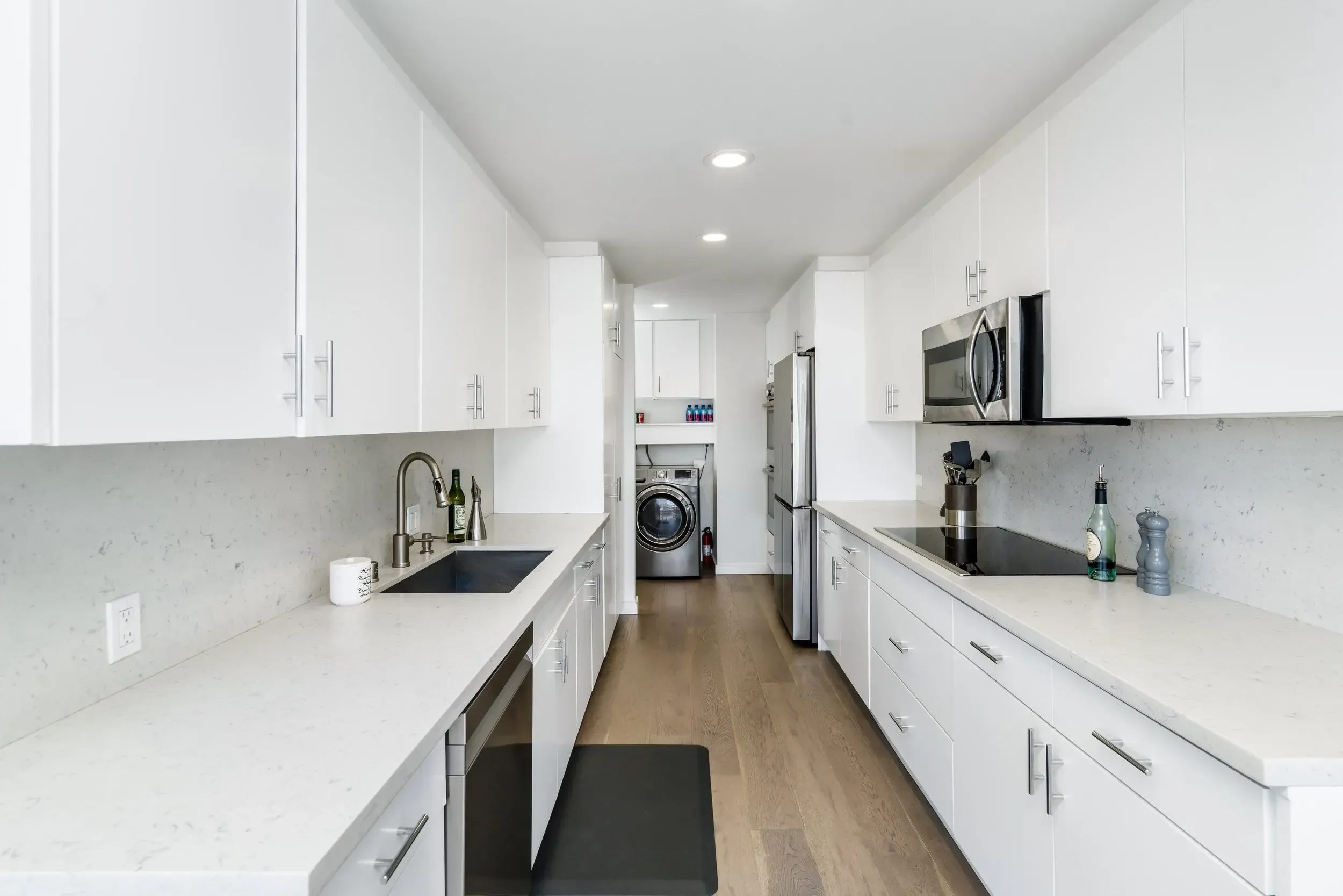 Modern white kitchen with marble countertops, stainless steel appliances, and wooden floors.
