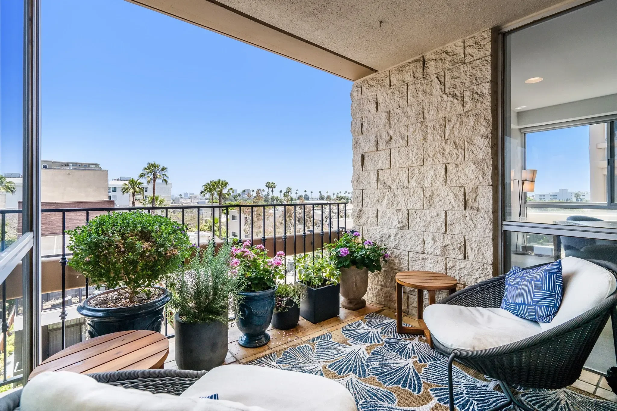 Balcony overlooking palm trees and nearby buildings with potted plants and outdoor furniture.