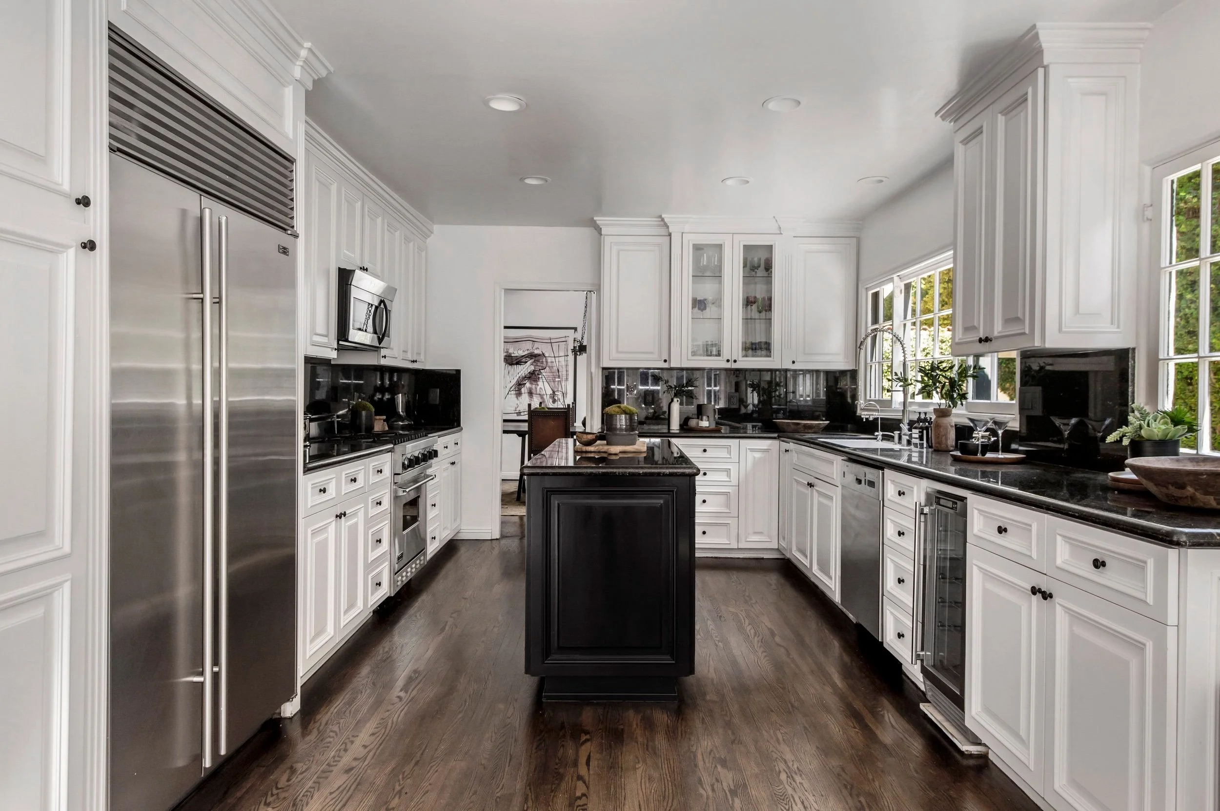 A spacious kitchen with white cabinets, black countertops, stainless steel appliances, and large windows bringing in natural light.
