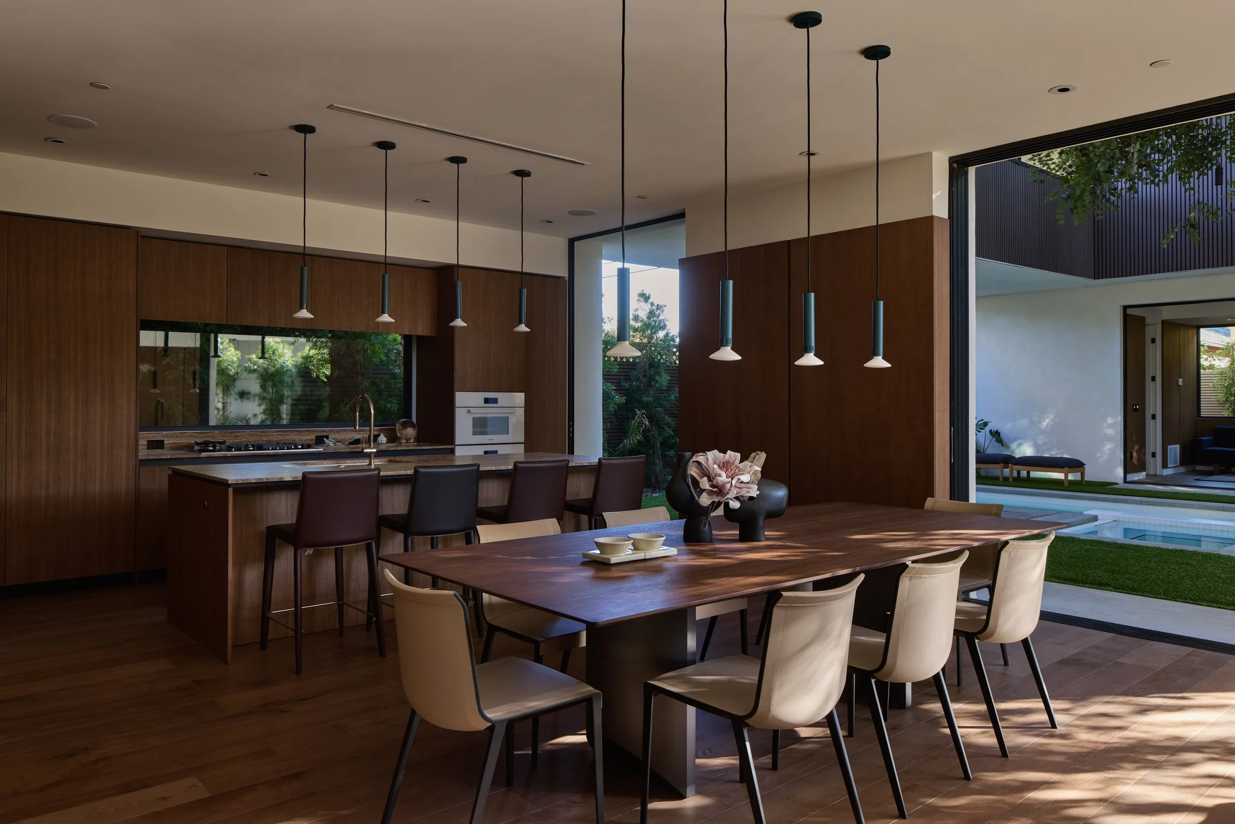 Modern kitchen and dining area with wooden cabinets, a large wooden dining table, and view of outdoor patio and greenery.