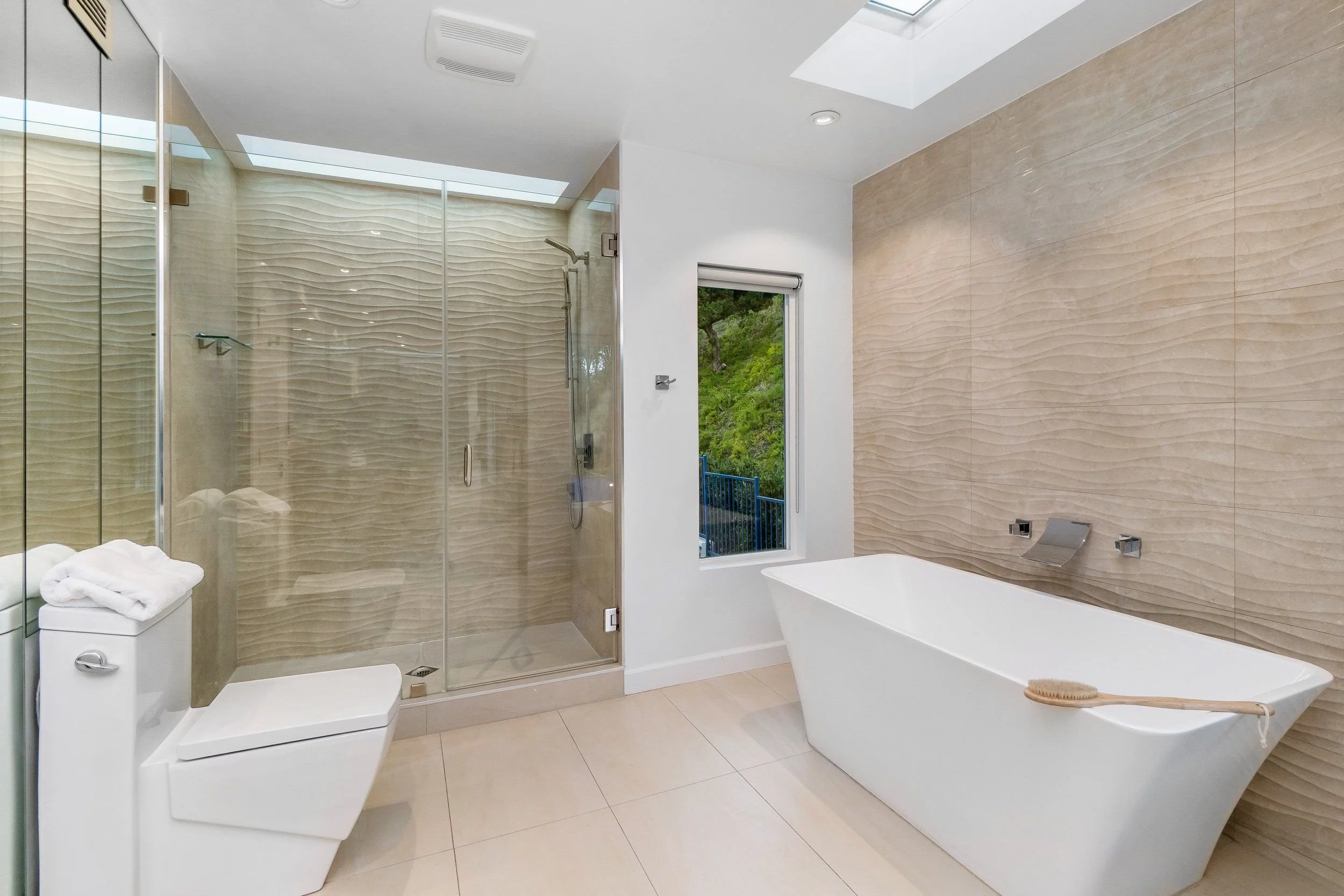 Modern bathroom with bathtub, walk-in shower with textured glass door, two windows, and beige textured wall tiles.