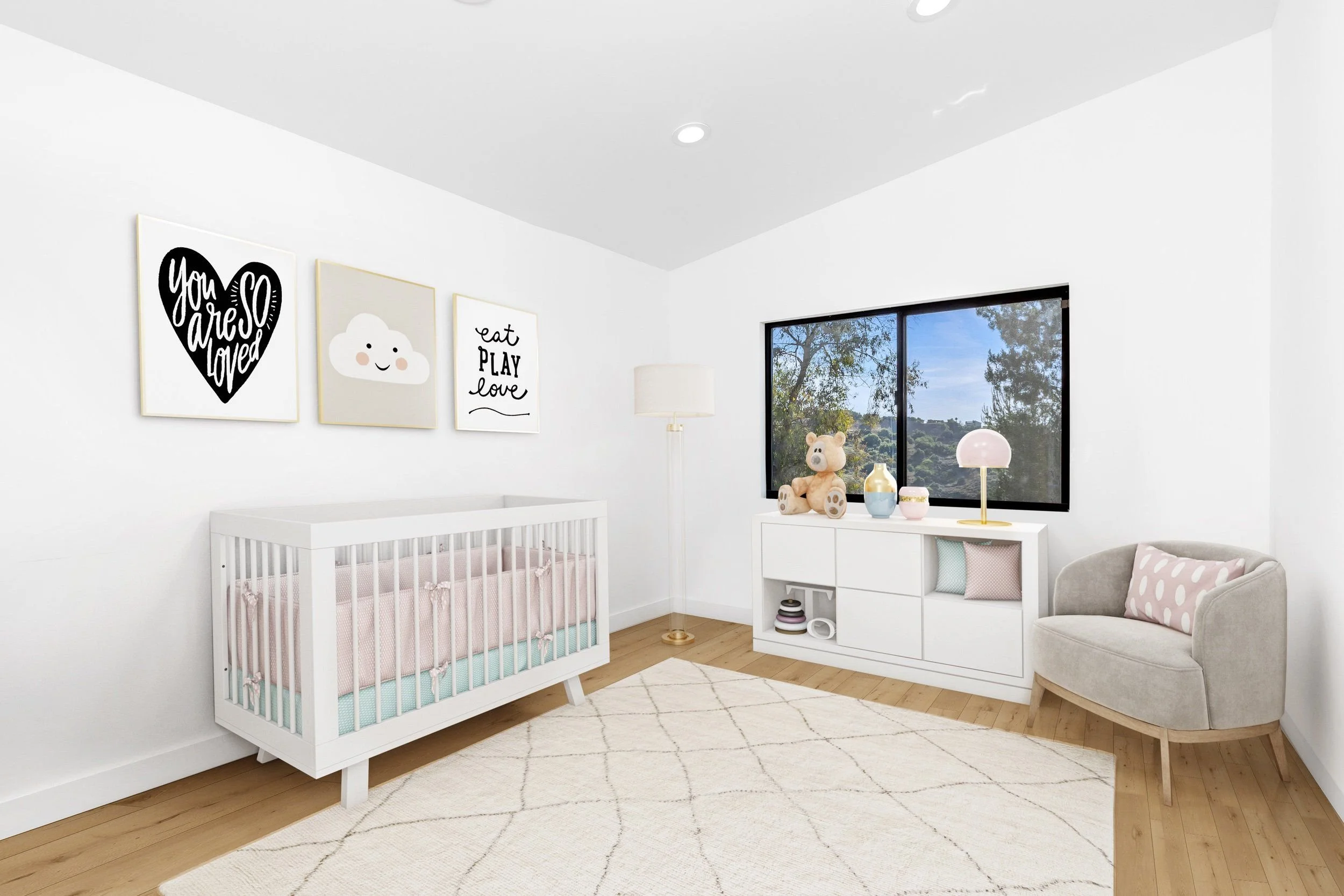 A baby's nursery with white walls, a changing table, wall art with positive messages, a window with a view of trees, and a cream-colored armchair with polka-dot pillow.