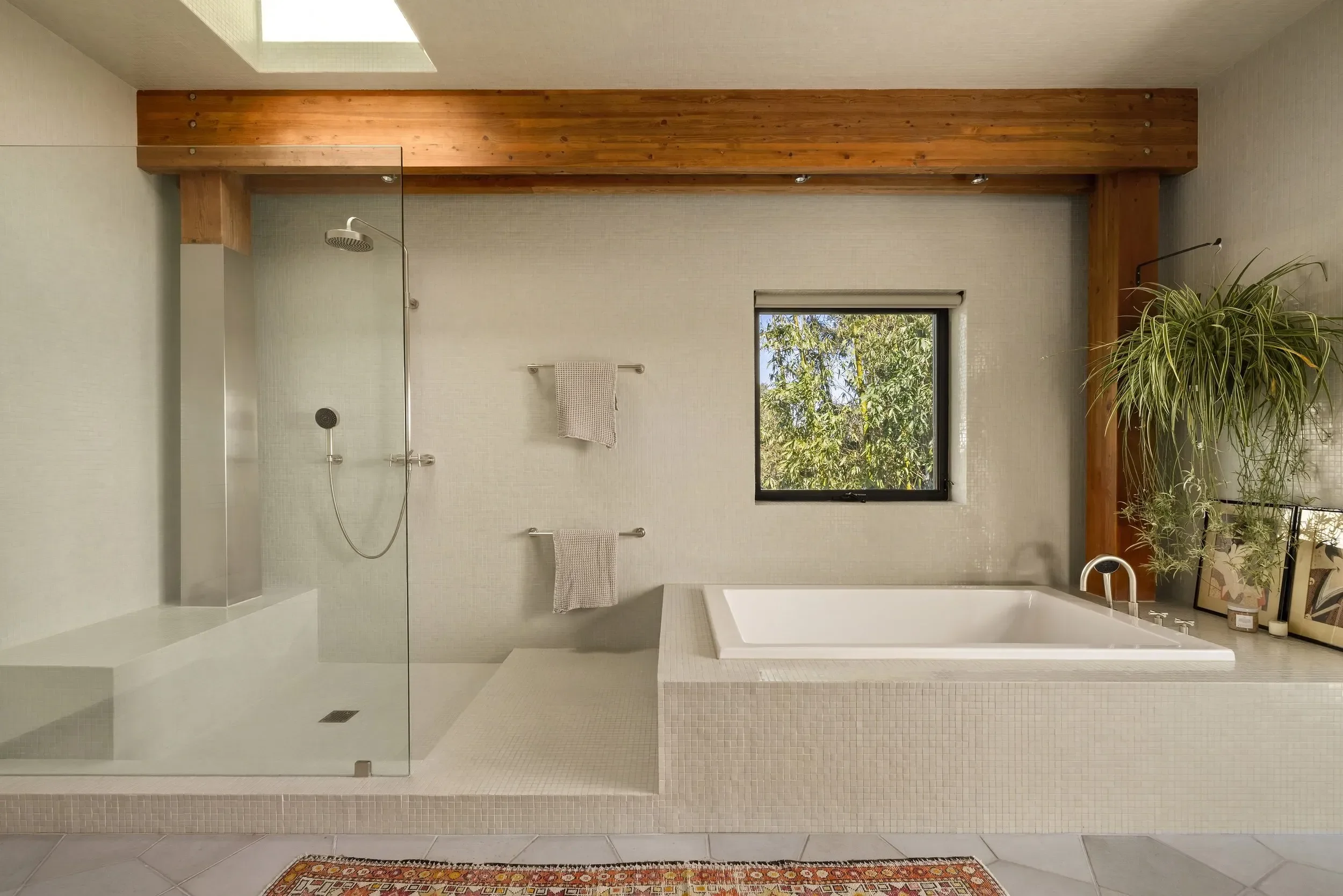 Modern bathroom with a walk-in shower, bathtub, large window showing green trees, and decorative plants on the side.