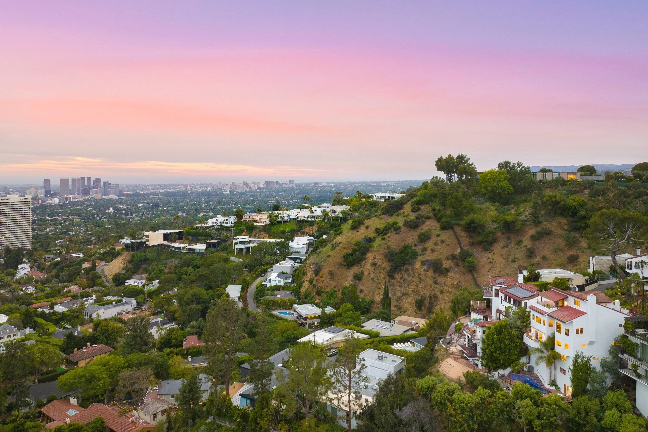 Urban skyline view with a hillside residential area and a cityscape in the distance during sunset with colorful pastel sky