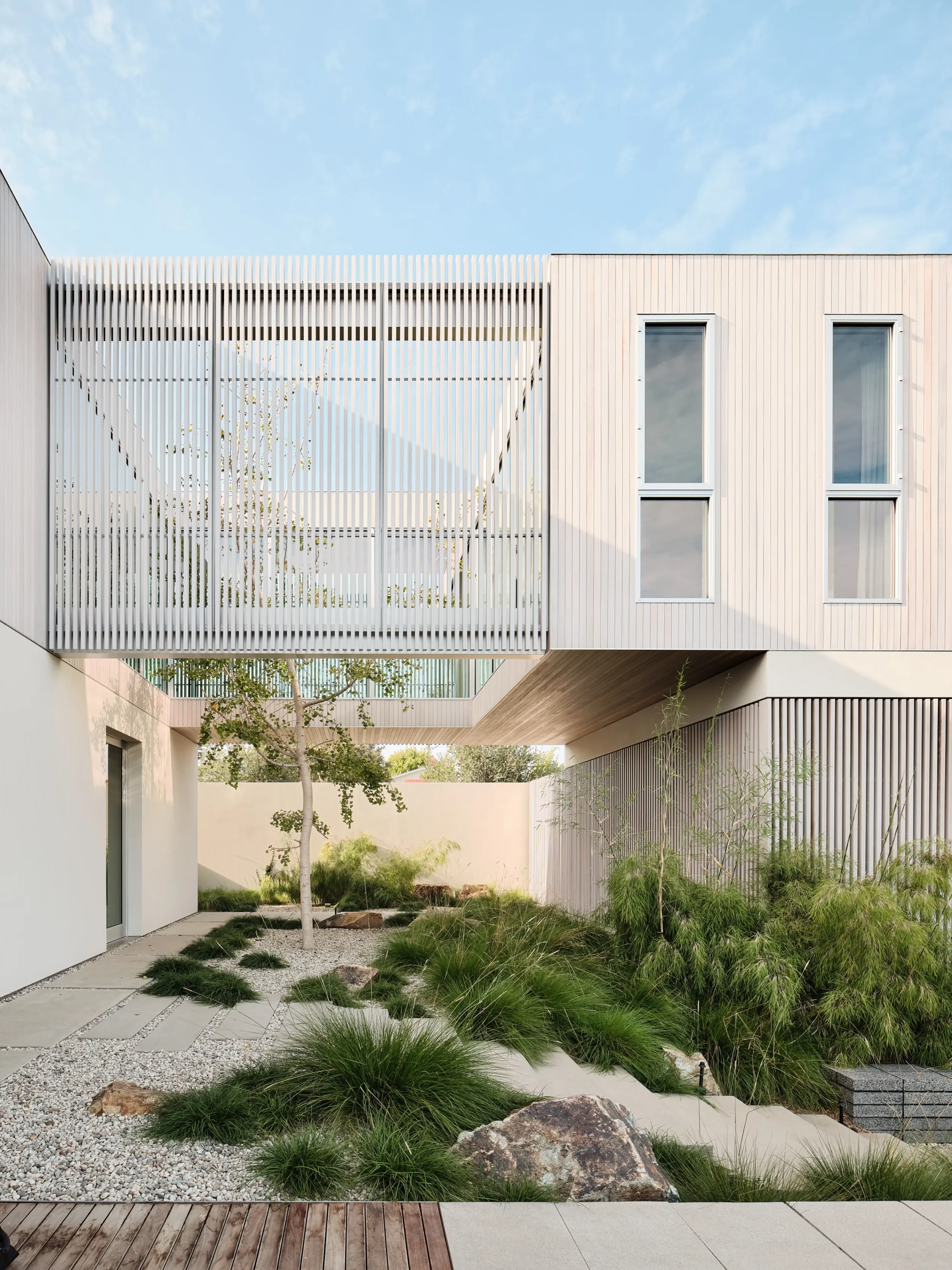 Modern architectural building with white exterior walls, large windows, and a courtyard garden with rocks, grass, and small trees.
