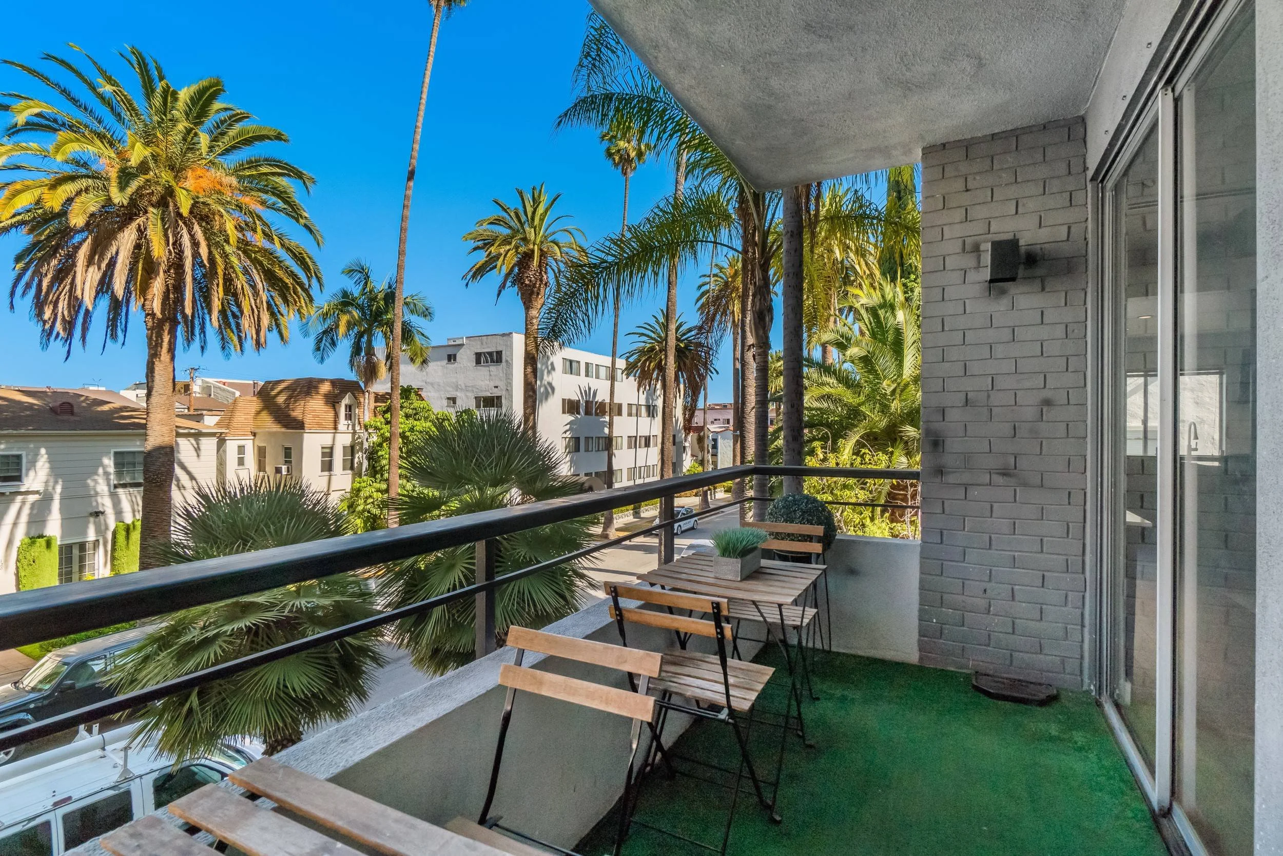Balcony view with palm trees, buildings, and a blue sky, featuring outdoor furniture including a table and chairs.