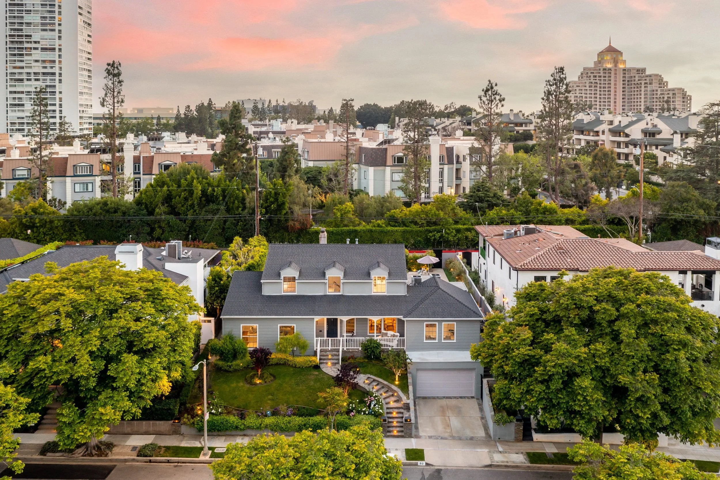 A residential neighborhood at dusk with a view of houses, trees, and a tall hotel in the background.