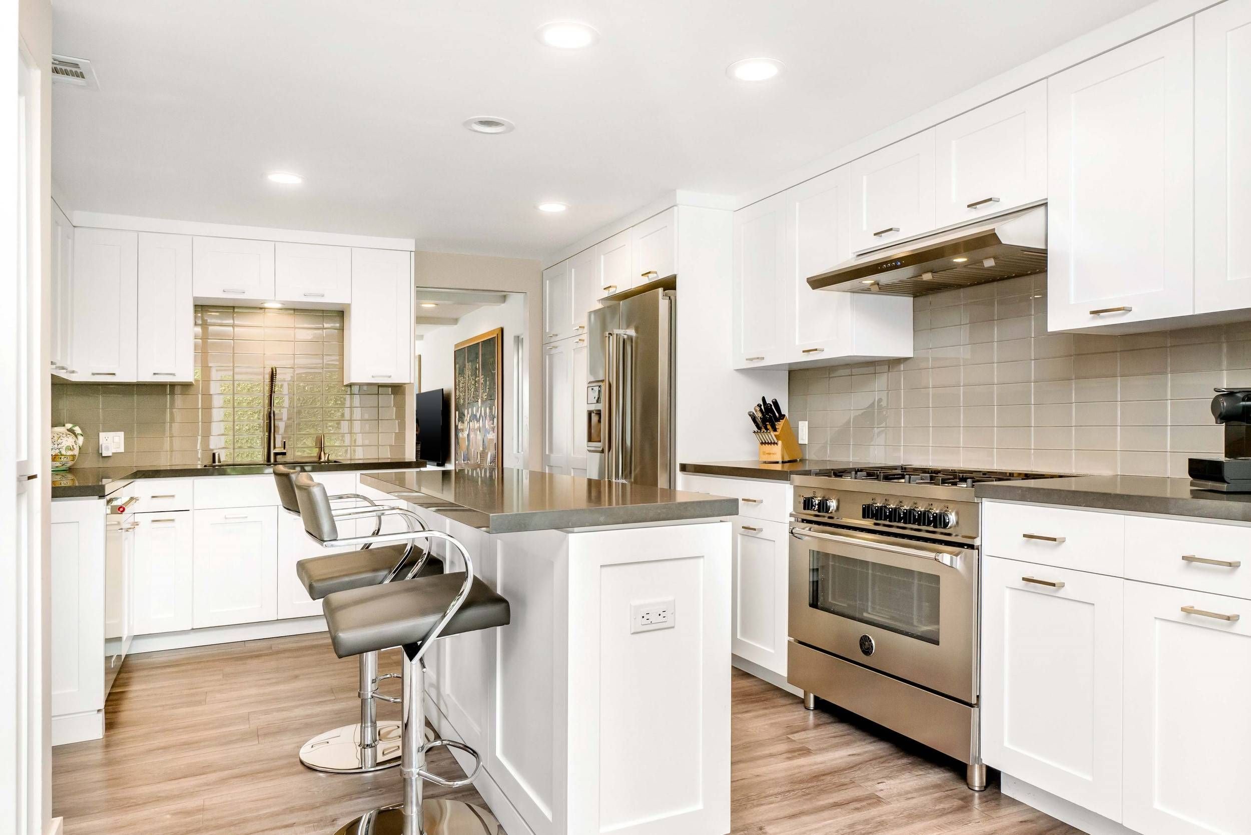 Modern white kitchen with stainless steel appliances, black countertops, and a central island with barstools.
