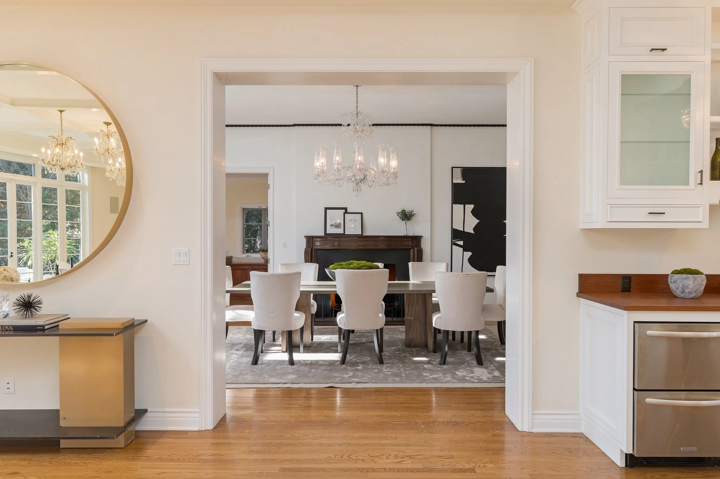 Dining room visible through an open doorway, featuring a wooden table with white chairs and a chandelier hanging from the ceiling.