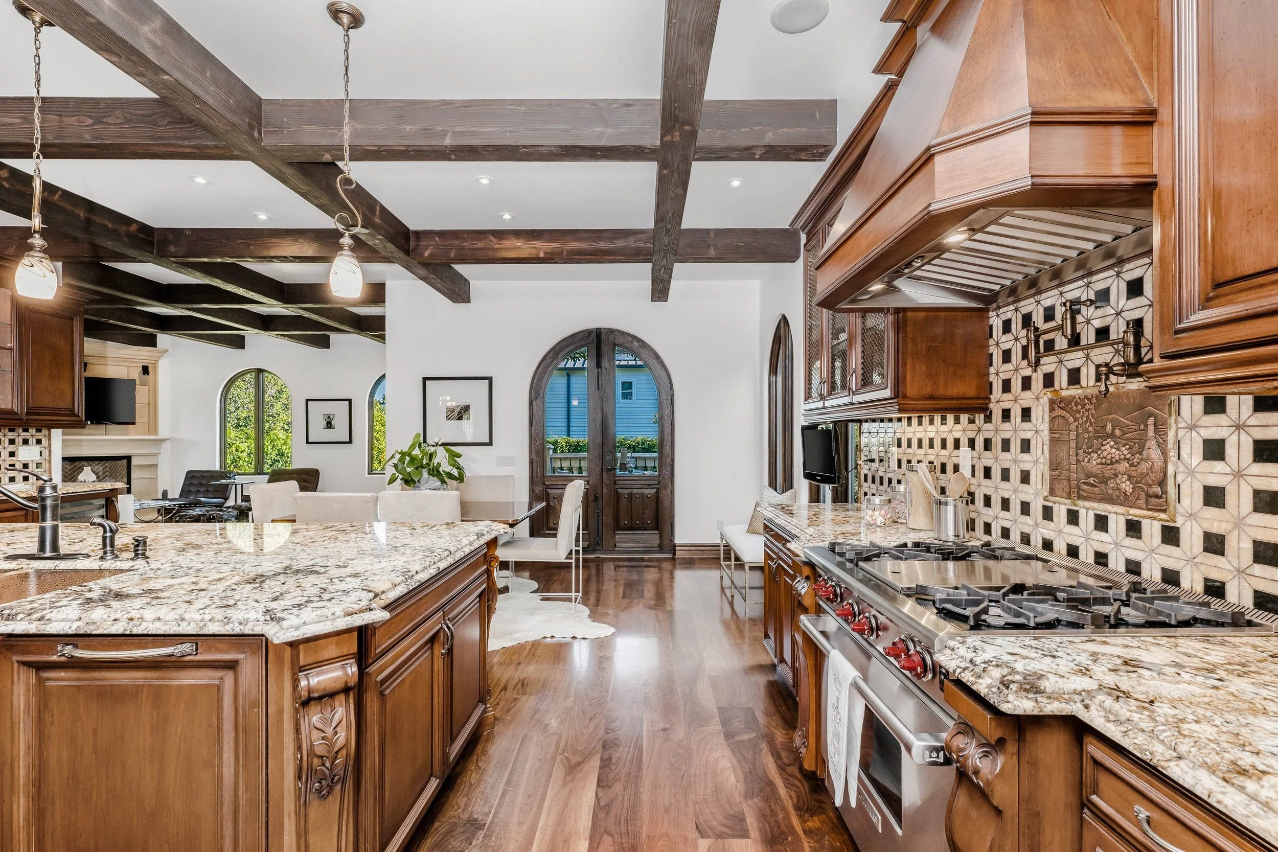Kitchen with wooden cabinets, granite countertops, a stainless steel stove, and decorative backsplash tiles. Visible dining area with chairs, windows, and a door leading outside.