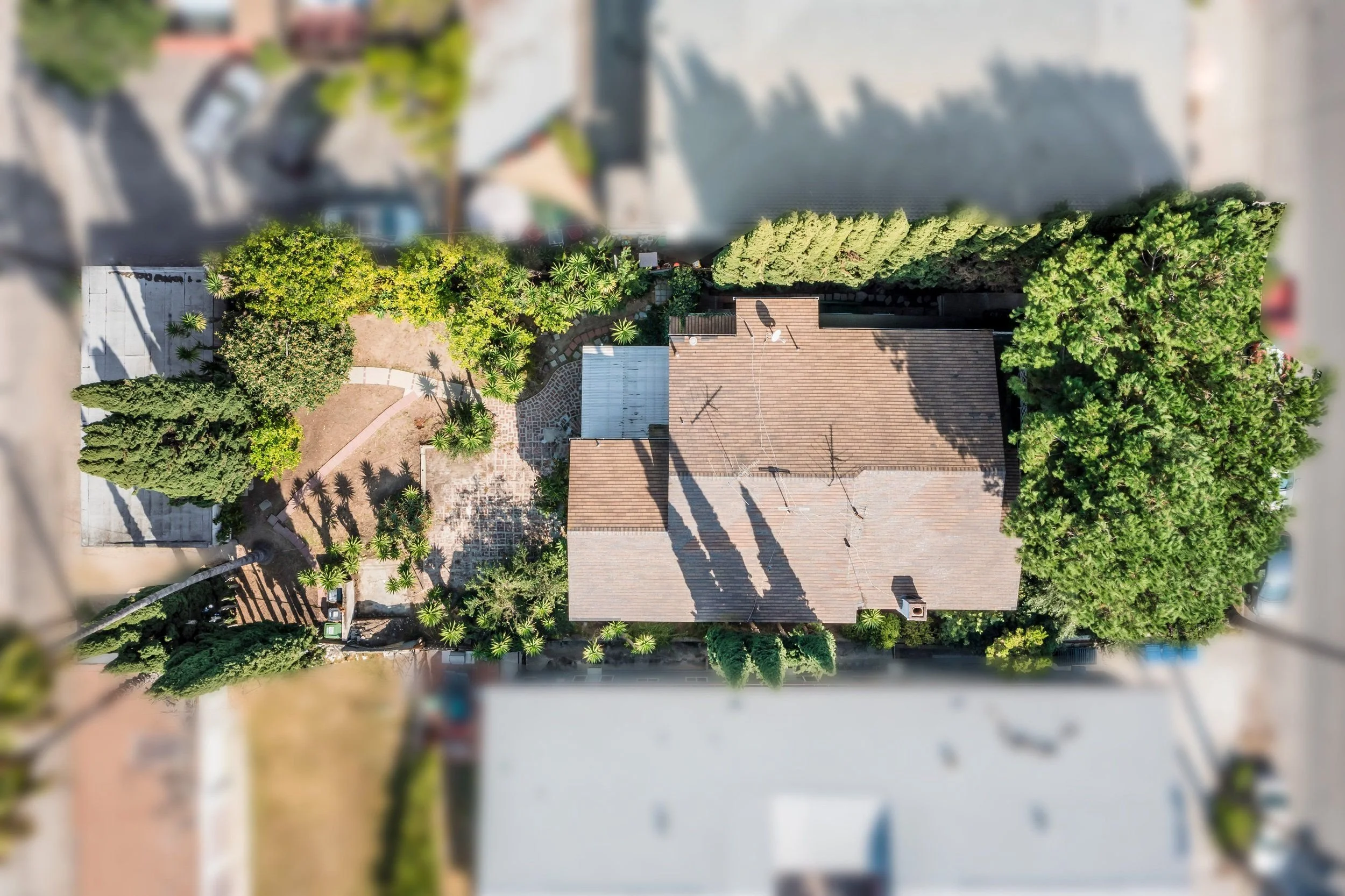 An aerial view of a residential house surrounded by trees and a garden with winding paths, captured from a drone or high vantage point.