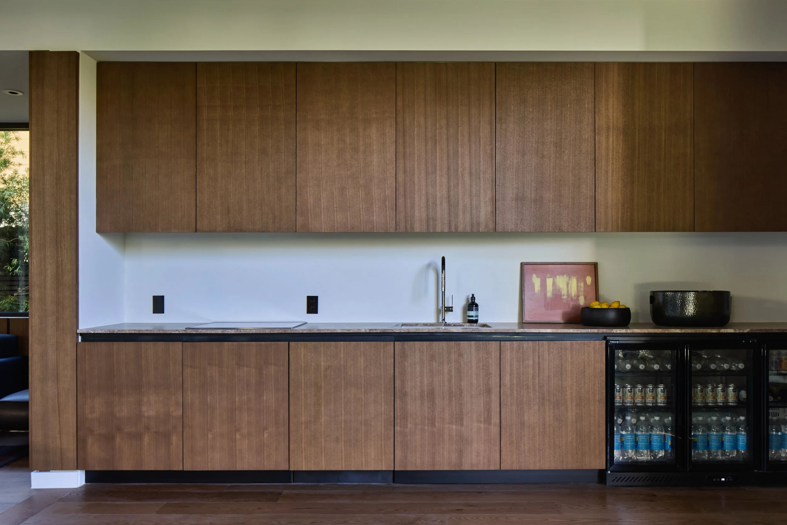 Modern kitchen with wooden cabinets, a white countertop, a black sink, a framed artwork, and a mini fridge with beverages.