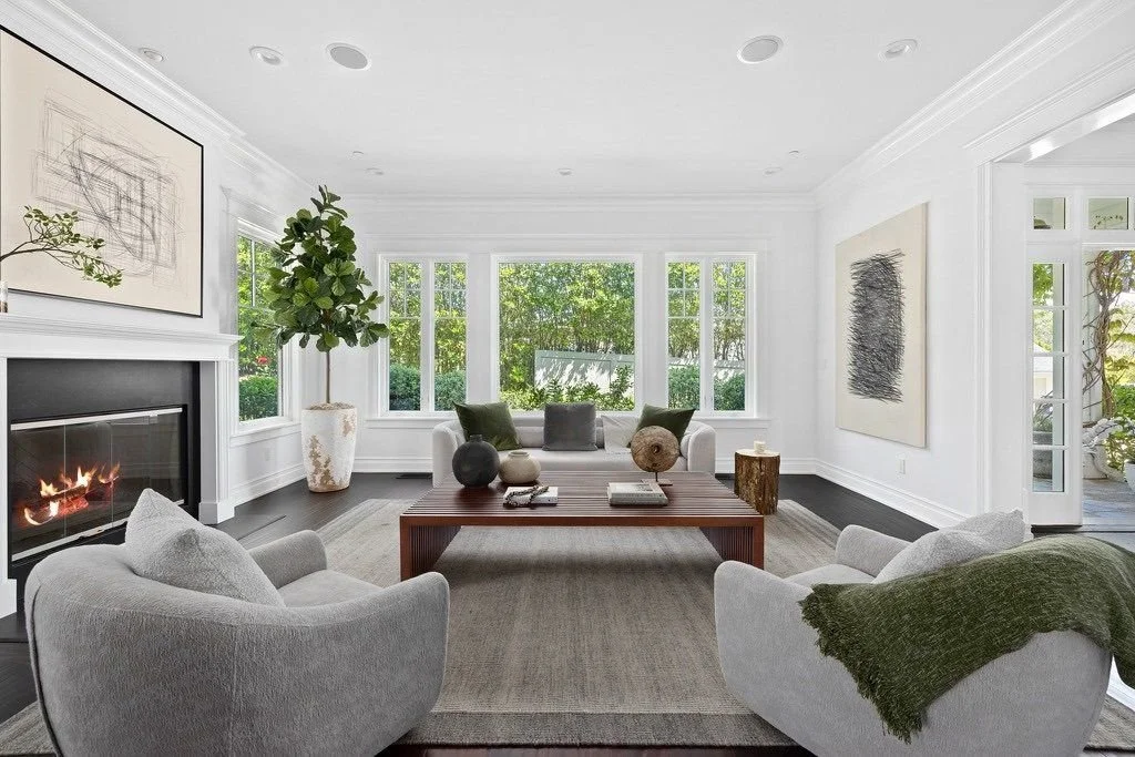 Bright living room with white walls, large windows, and modern decor including a fireplace, abstract artwork, a potted plant, and a beige sofa.