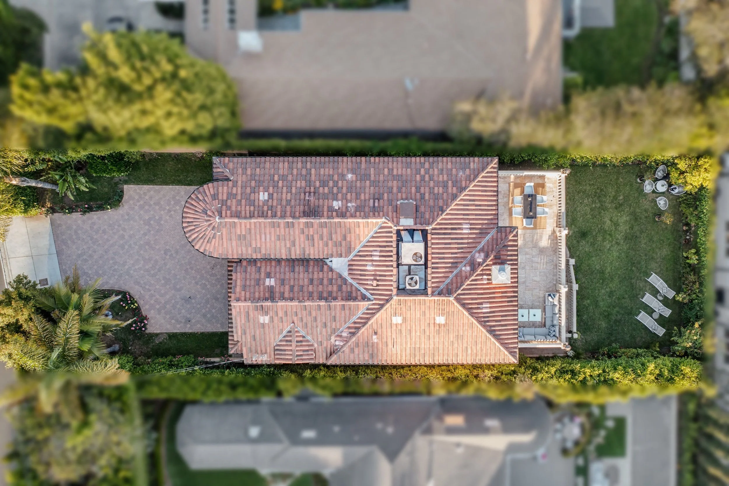 Aerial view of a house with a tiled roof, backyard patio, outdoor furniture, and surrounding greenery.