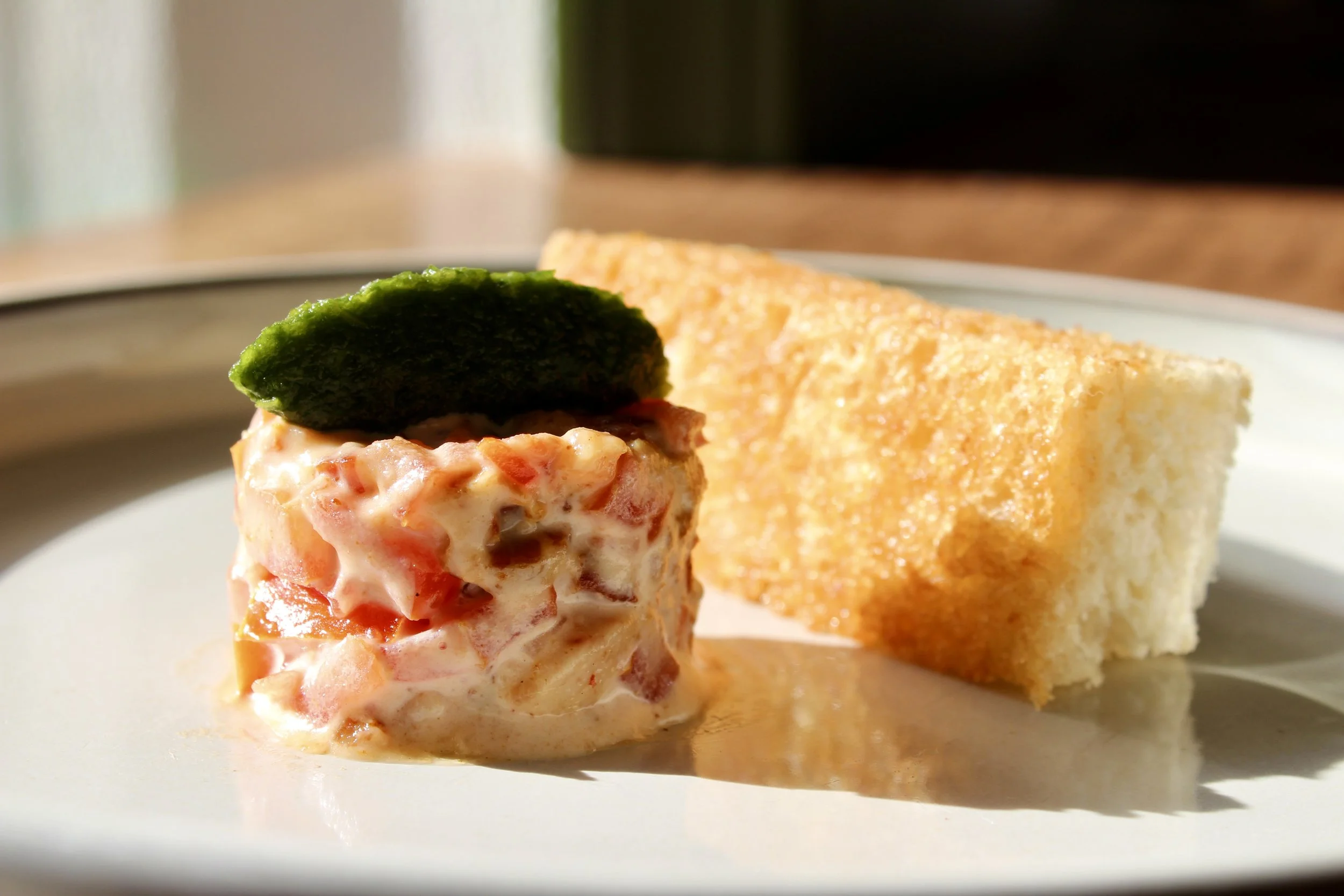 A serving of shrimp salad topped with a pickle, served with a slice of garlic bread on a white plate.
