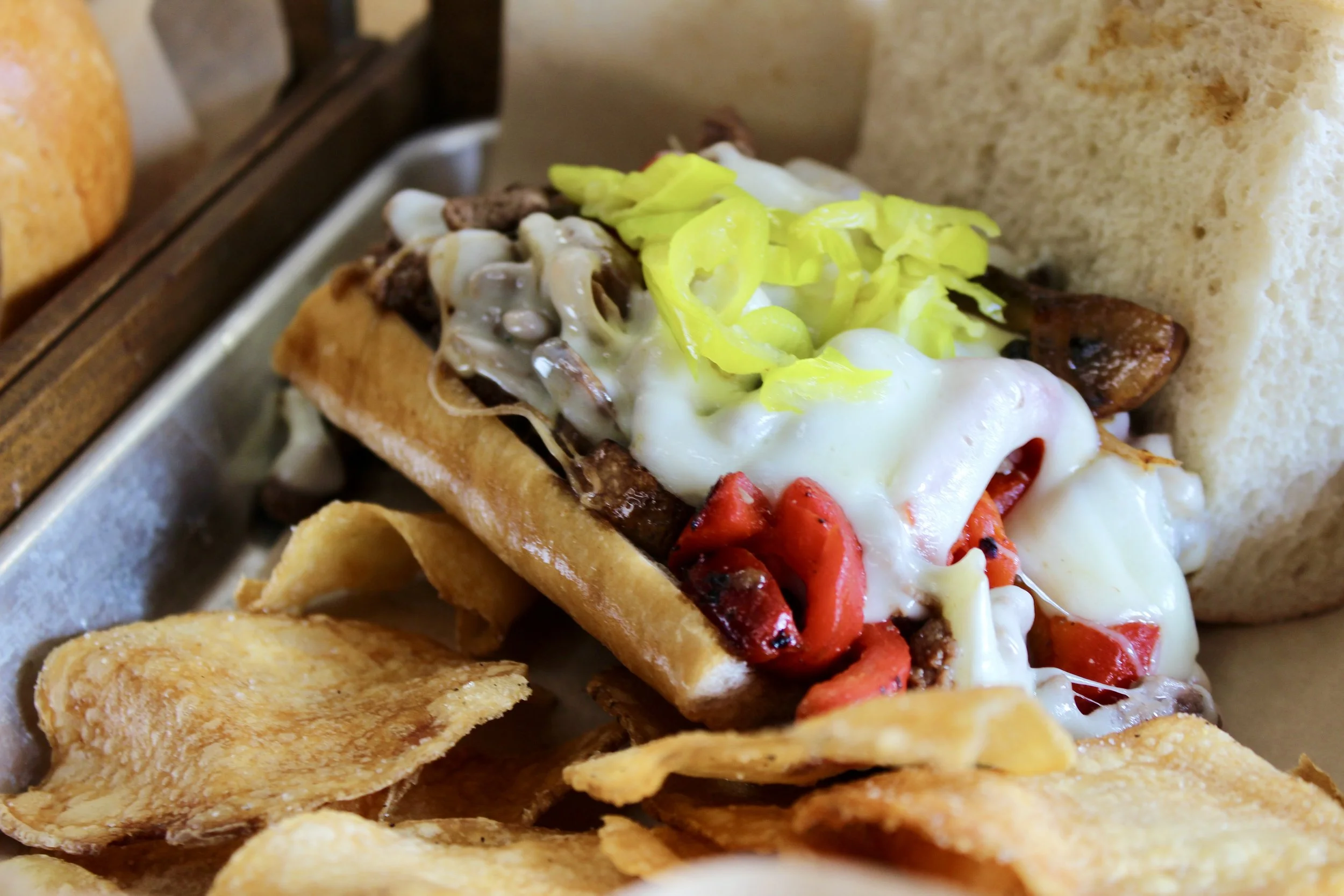 Chili cheese dog with shredded lettuce, chili, melted cheese, and red peppers in a bun, with potato chips on the side.