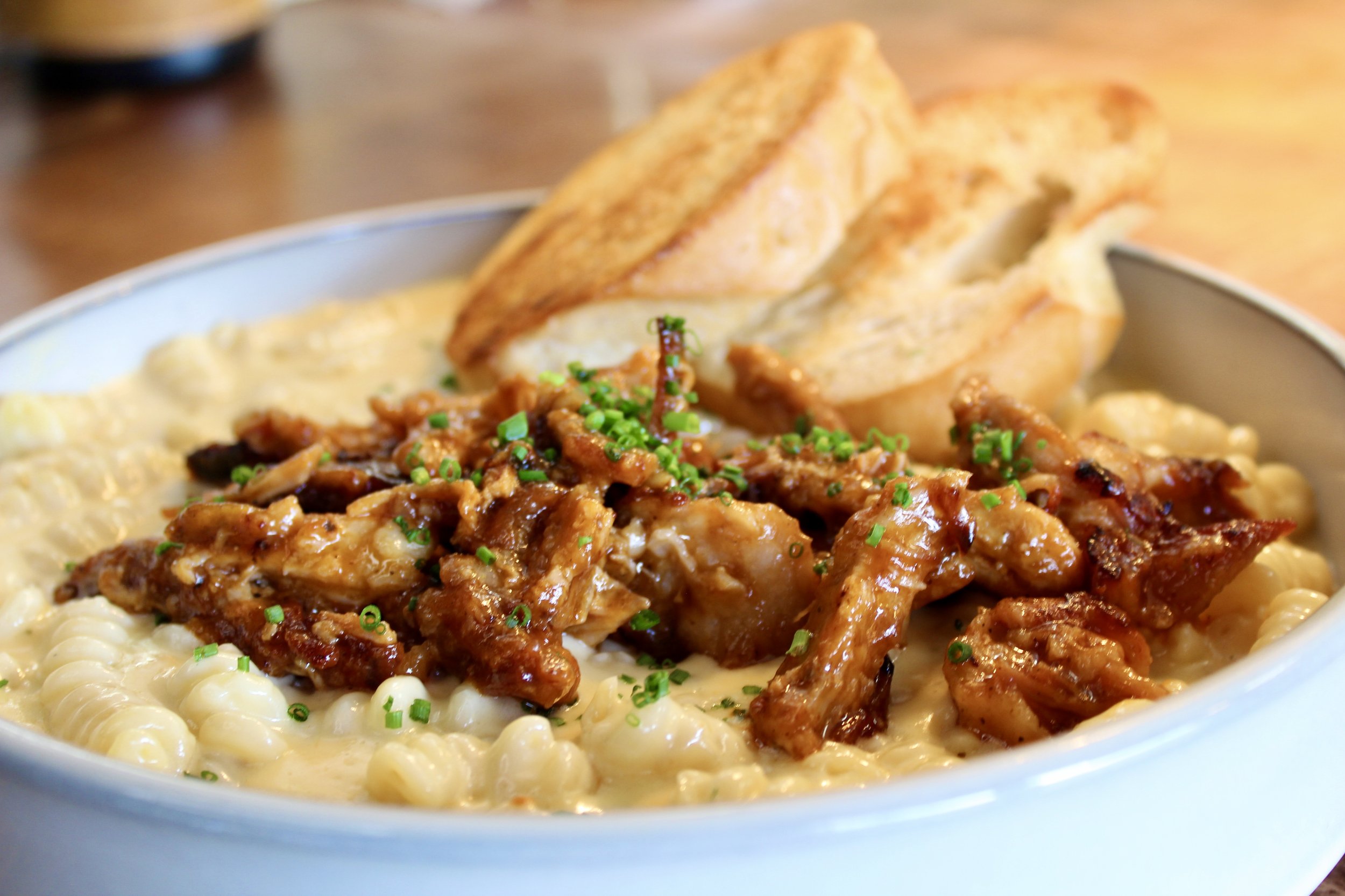Creamy macaroni and cheese topped with shredded chicken, chopped chives, and two pieces of toasted bread in a bowl.