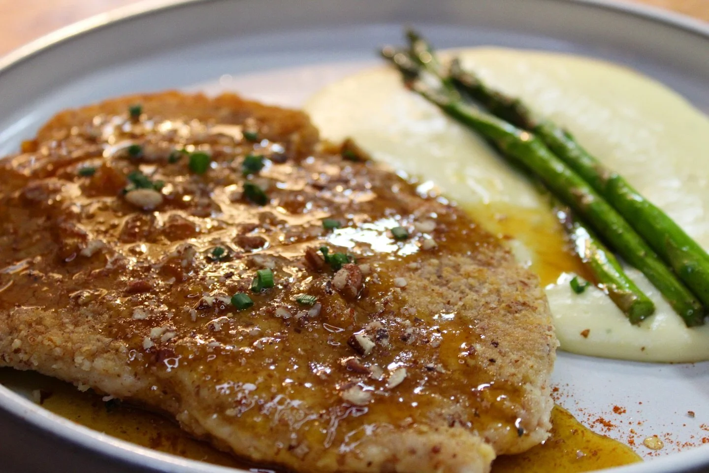 A plate of grilled chicken topped with sauce and chopped herbs, served with mashed potatoes, steamed asparagus, and sprinkled spices.