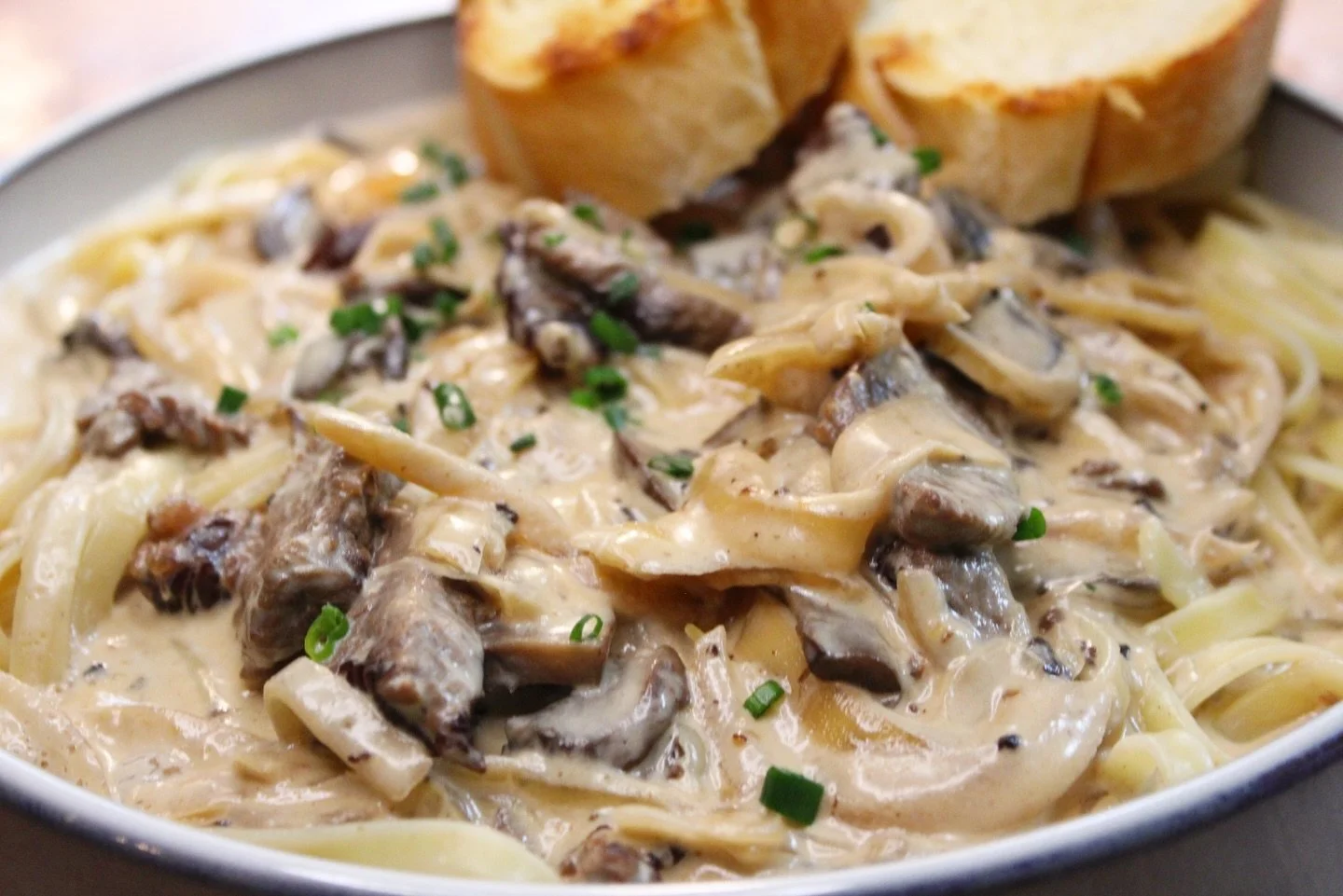 Fettuccine pasta with creamy mushroom sauce and sliced toasted bread on the side.