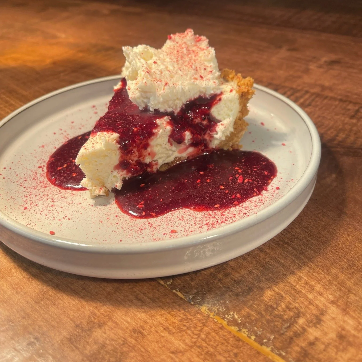 Slice of cheesecake with berry topping and sauce on a white plate