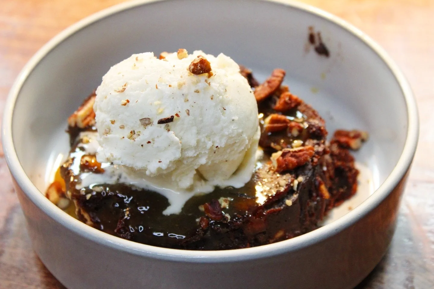 A bowl of warm chocolate brownie topped with a scoop of vanilla ice cream and chopped nuts.