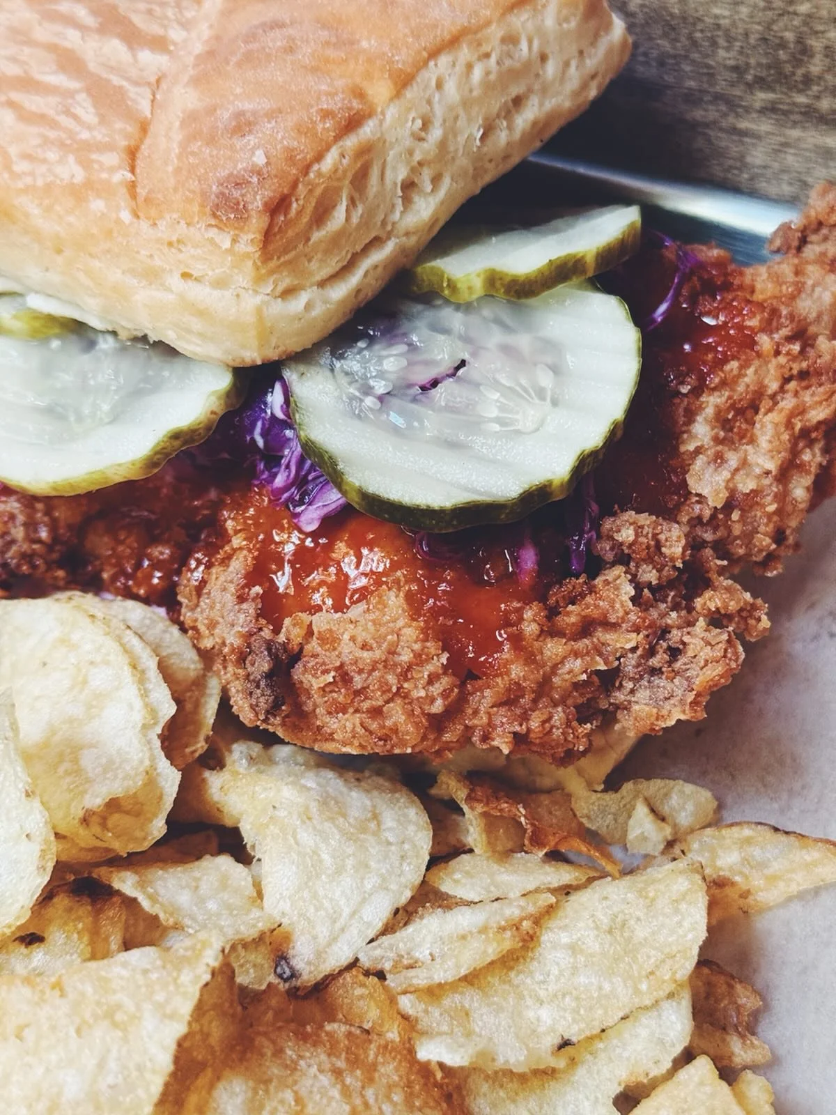 Close-up of fried chicken sandwich with pickles on top, surrounded by potato chips.