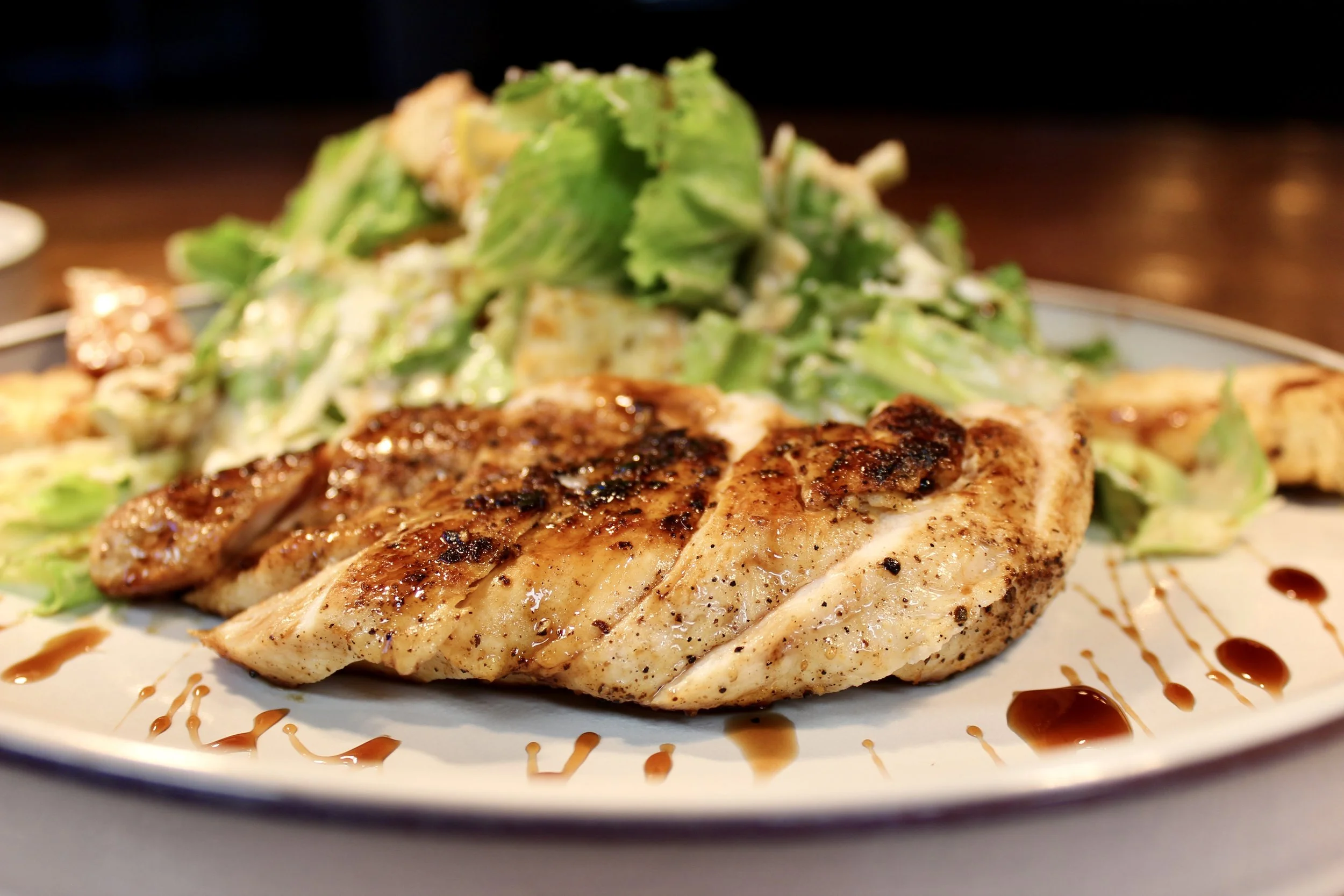 Grilled chicken breast with a side salad of lettuce and tomatoes, drizzled with balsamic glaze.