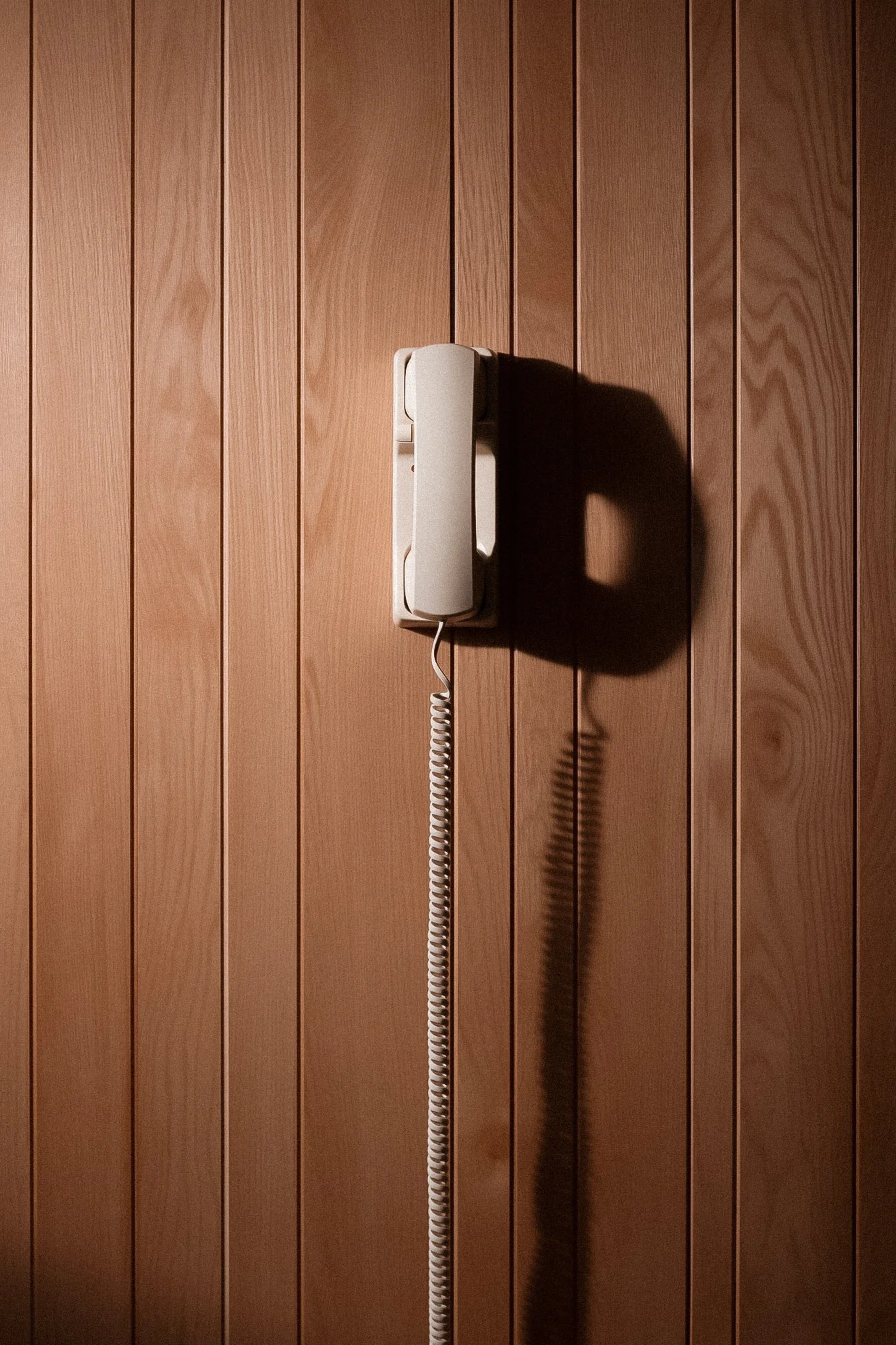 Wall-mounted landline phone with a coiled cord, cast shadow on a light wood-paneled wall. Therapy private practice office space in Ritchie Edmonton, AB. Offers in-person and virtual therapy and assessment services.