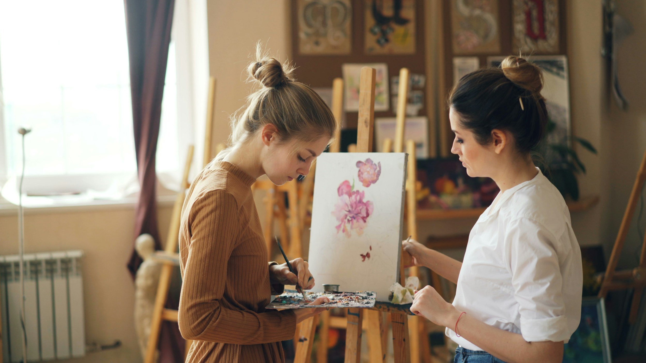 Two women painting on canvases in an art studio.