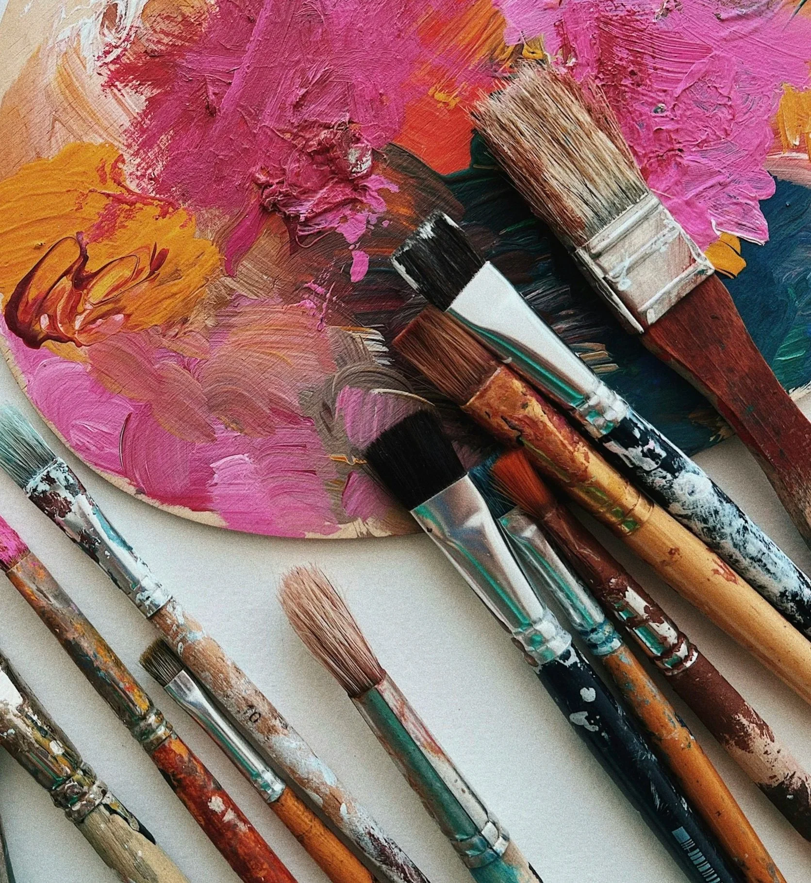 Paintbrushes resting on a colorful palette with pink, orange, blue, and green paint.