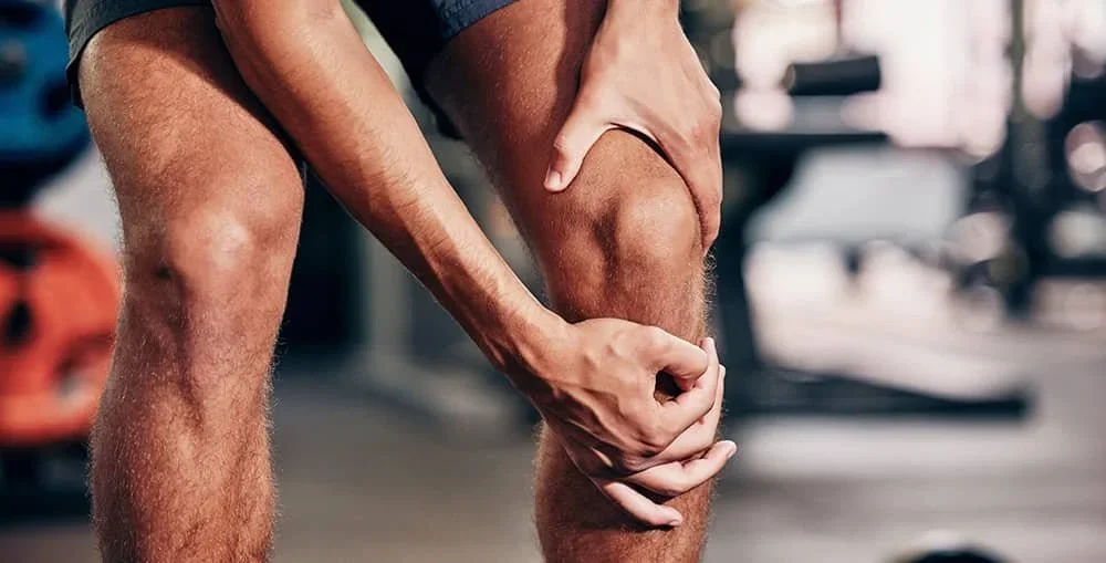 A person is holding their injured knee at the gym.
