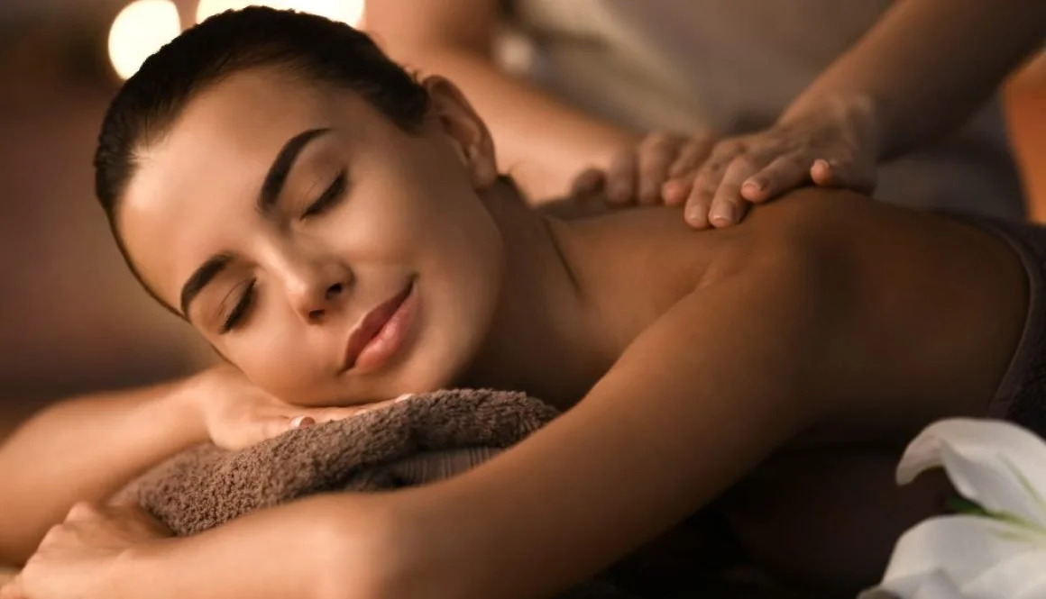 A woman receives a massage and is lying face down with a pillow under her head, her eyes closed, looking relaxed and content.