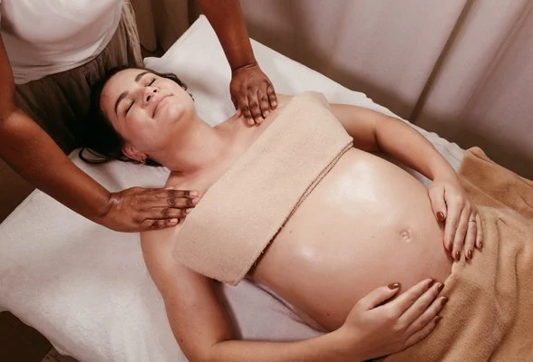 Pregnant woman receiving a massage on her shoulders and stomach while lying on a massage table