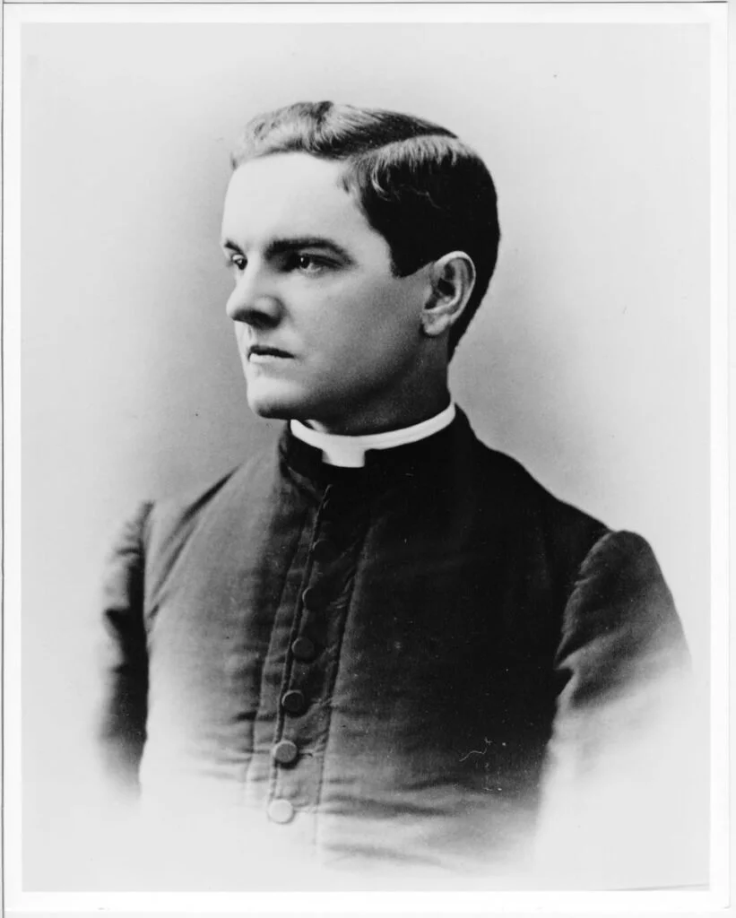 Black-and-white portrait of a Catholic priest in cassock with Roman collar, facing to the side