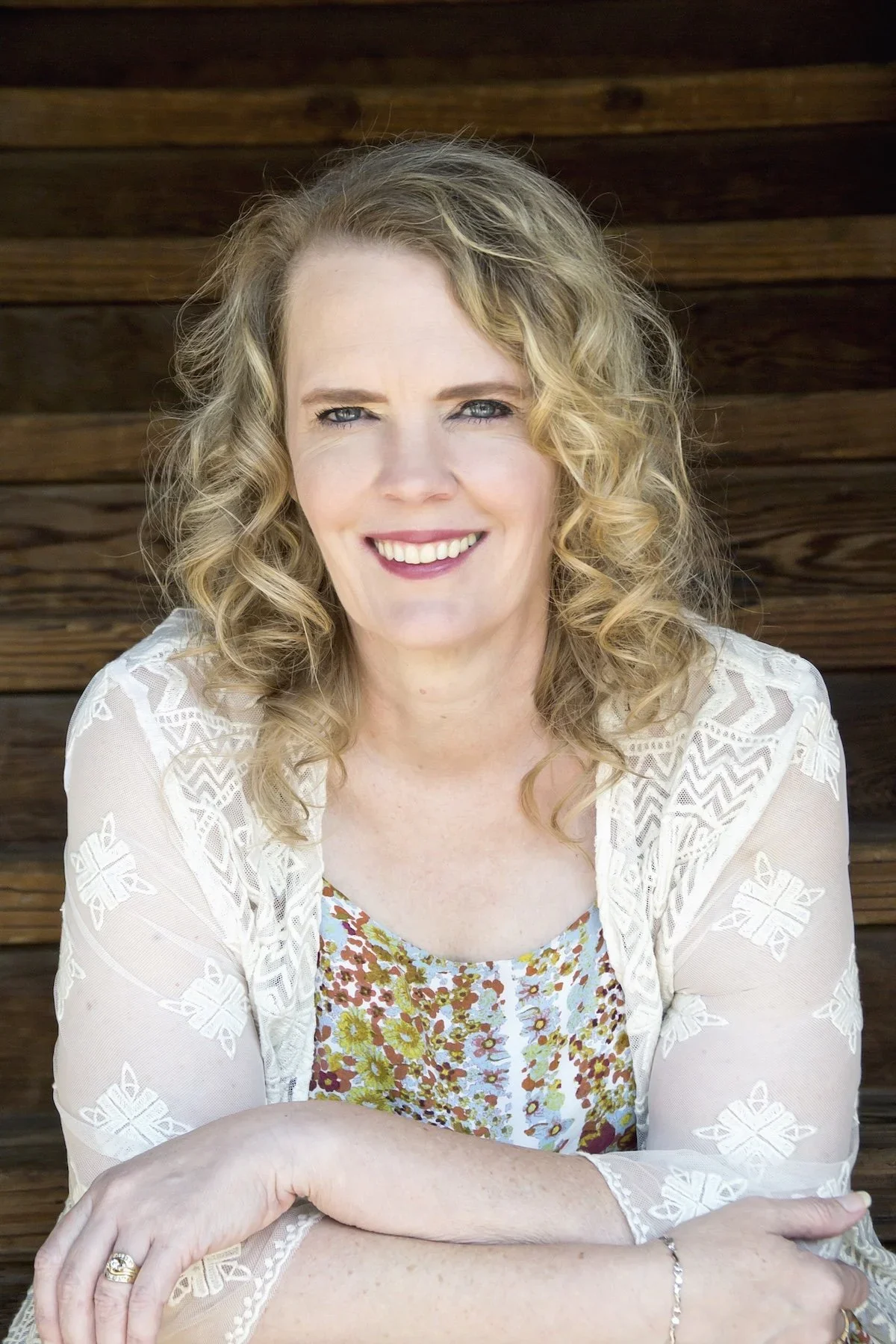 Headshot of Rhonda Parish , Vice President of. the WCCMA. She is blonde with bright blue eyes and wearing a lace top with yellow and blue flowers. She is leaning forward with her arms crossed.
