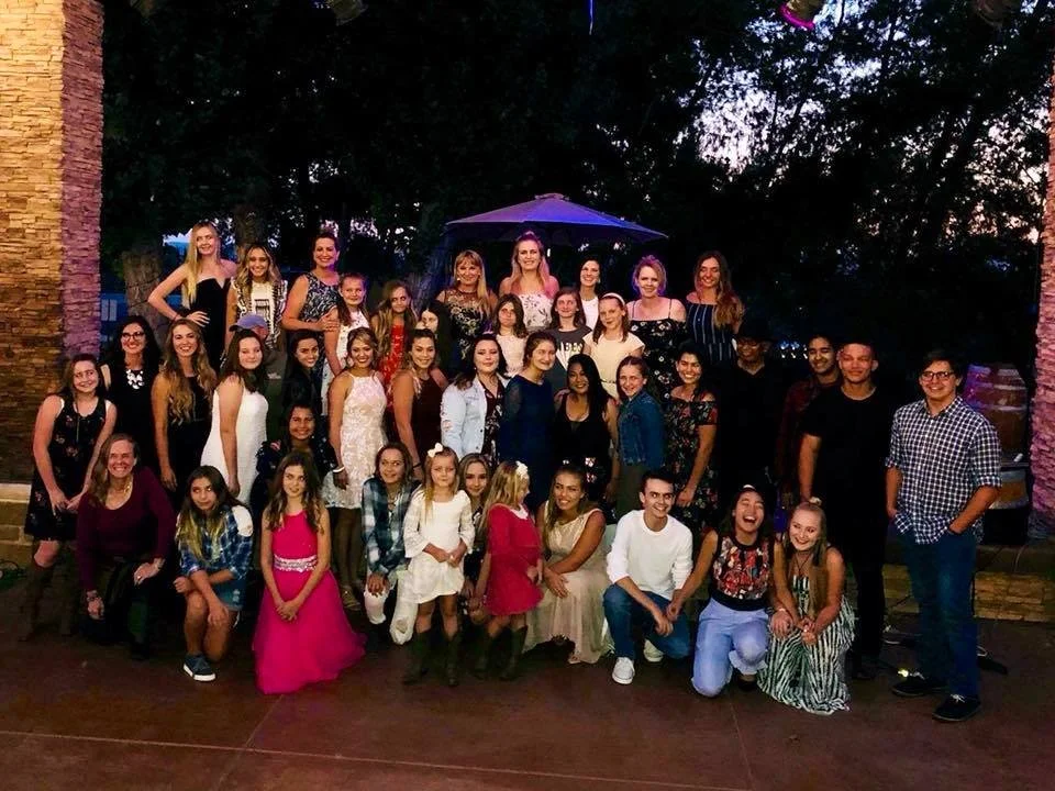 Group of young women and men posing outdoors at night, some wearing dresses, in front of brick columns and trees at the annual Hot August country music competition award show