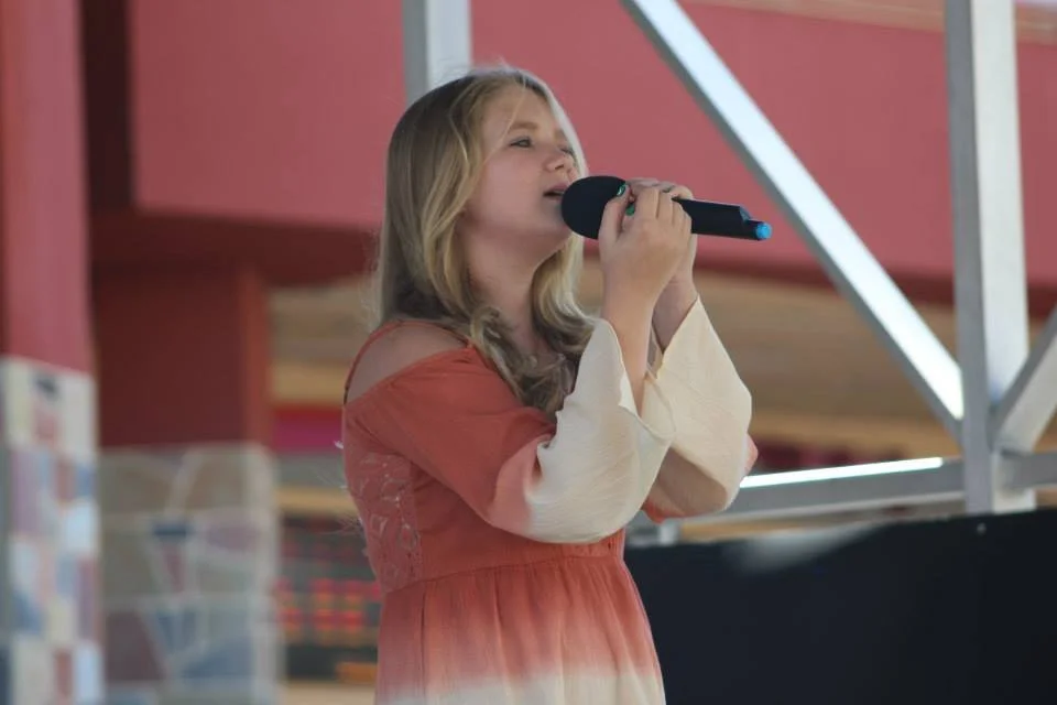 A young woman in a red dress holding a microphone on stage at the annual West Coast Country Music Association Hot August country music competition