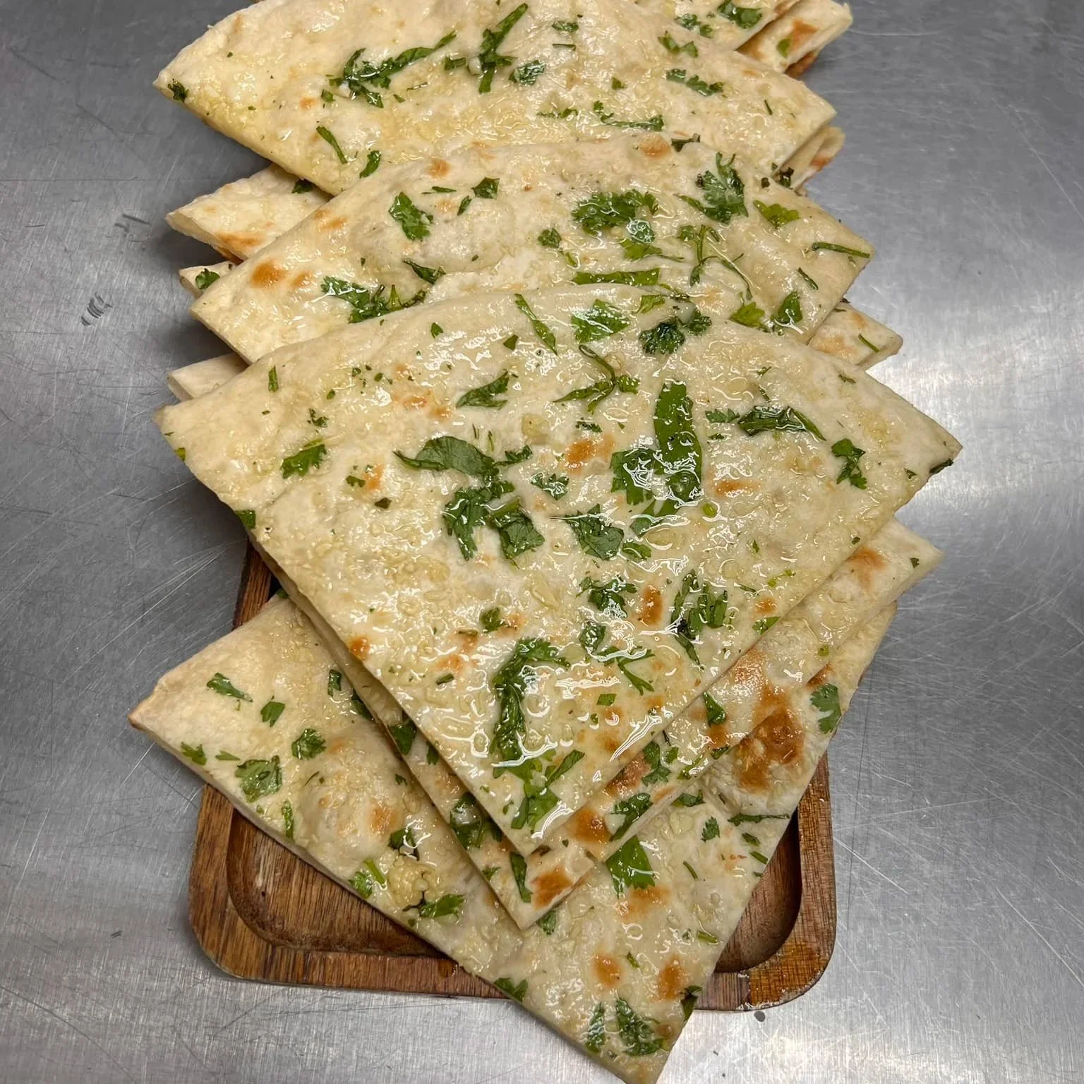 Slices of flatbread with chopped herbs and a drizzle of oil on a wooden board.